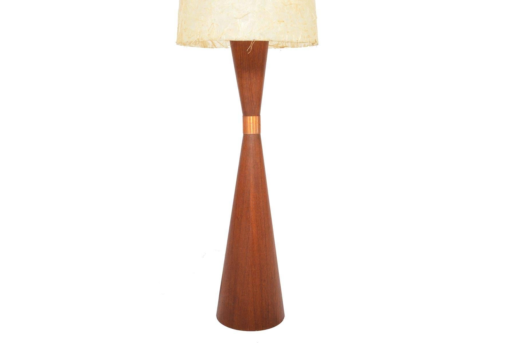 This beautiful Italian modern teak hourglass floor lamp was designed in the 1960s. The base is weighted for a sturdy yet elegant Silhouette. A copper cuff sits in the centre. Original paper shade provides a warm glow. In excellent original condition