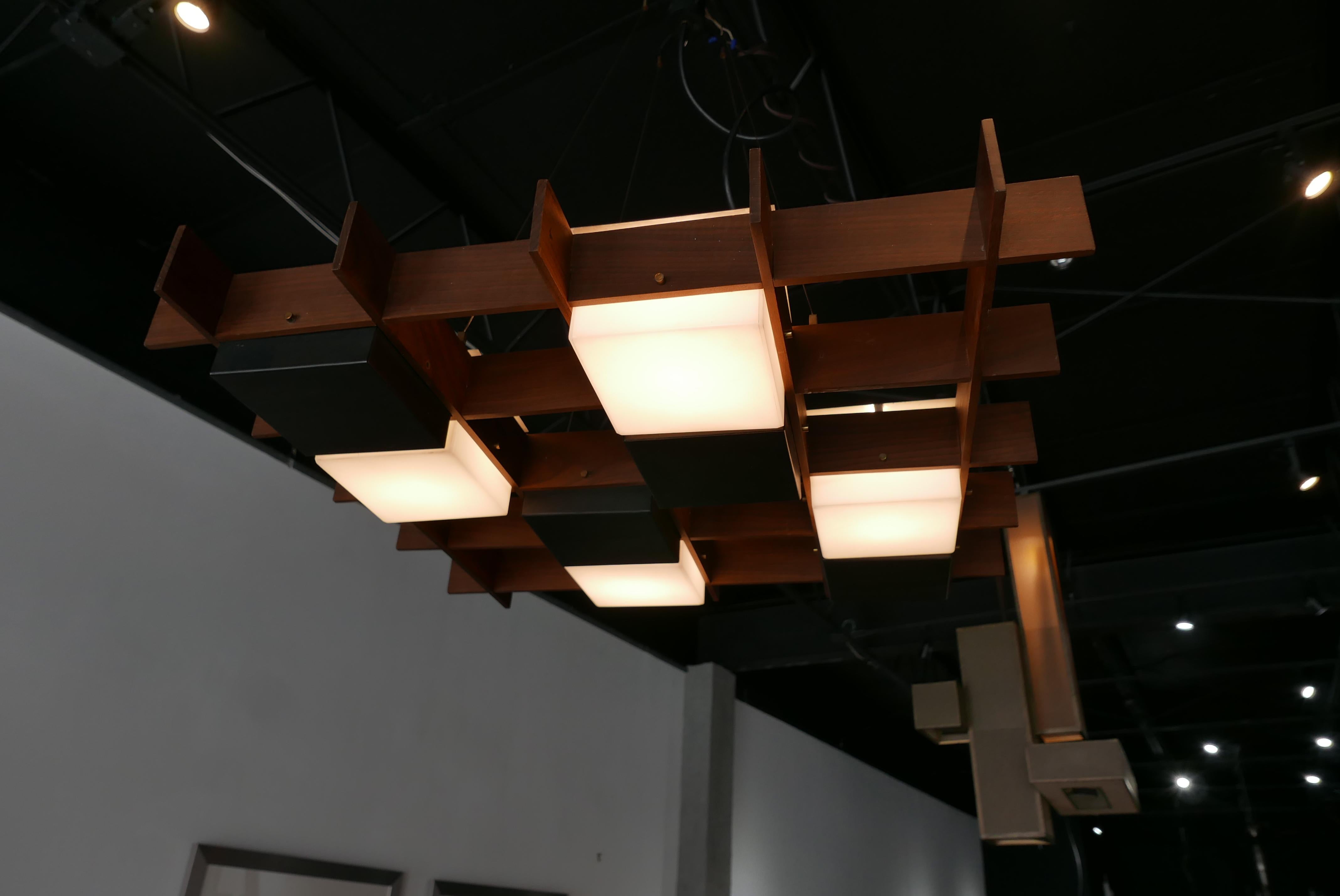 This Angelo Brotto chandelier is a beautiful example of Mid-Century Modern lighting, combining a wooden grid with recessed metal and Lucite lenses that fit into the grid pattern. The black and white alternating pieces create a very dynamic and