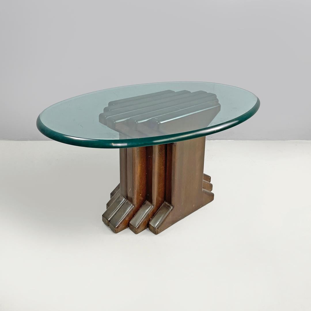 Italian modern wooden coffee table with geometrical base and glass top, 1970s
Coffee table with an oval top in transparent glass tending towards blue. The central stem is made of wood and is composed of staggered strips that grow and decrease