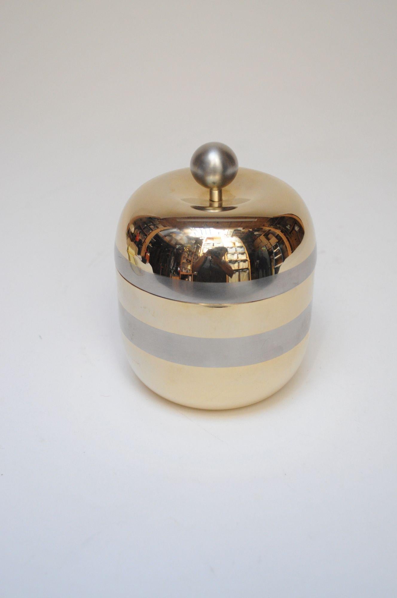 Cajita en forma de manzana para guardar pequeños objetos, de aluminio dorado con bandas plateadas y asa en forma de orbe (años 60, Italia).
Lujoso objeto decorativo en muy buen estado, recién pulido, del que sólo queda una ligera pátina/desgaste