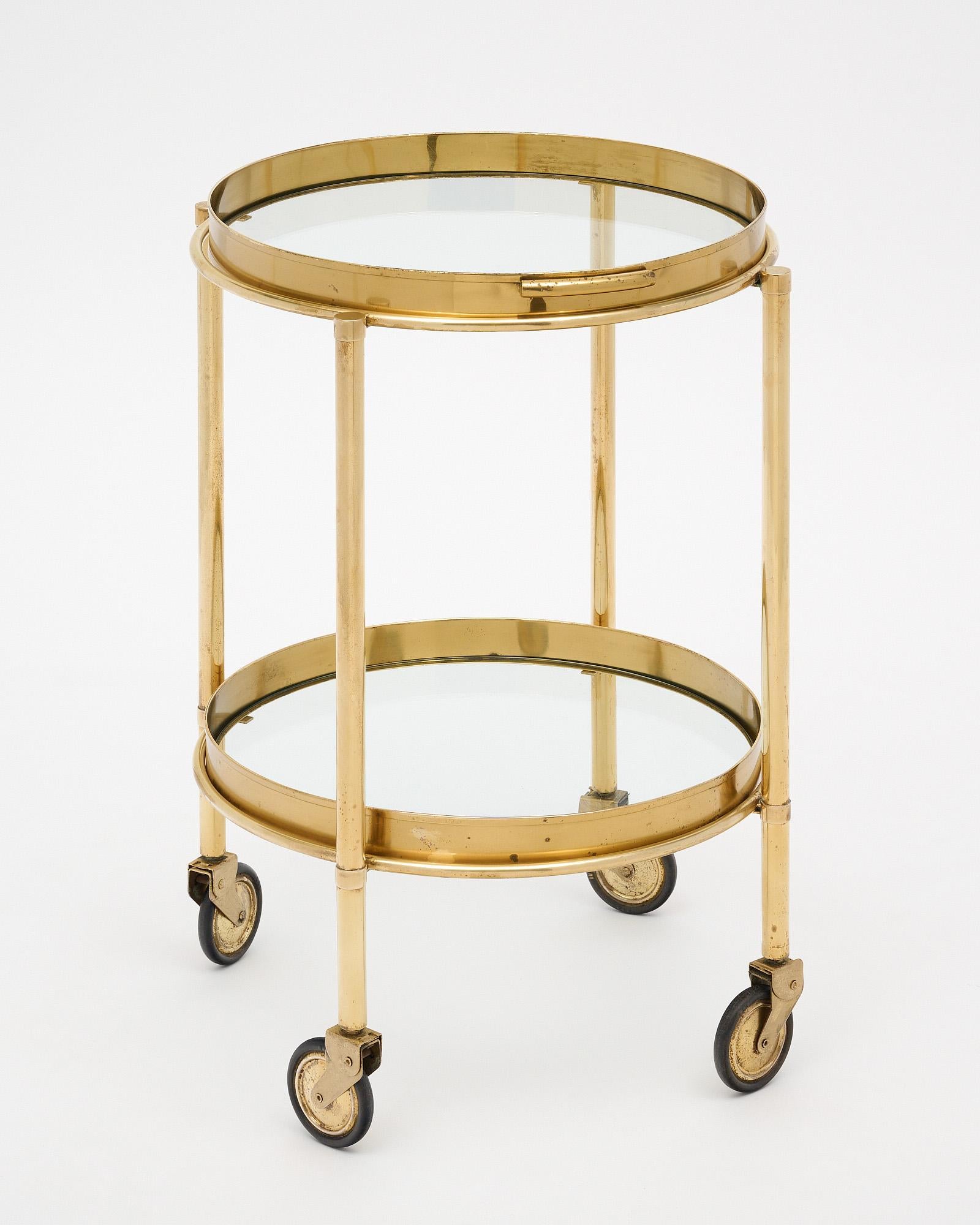Bar cart from Italy in the Modernist style. This piece is made of brass with a circular frame and four supportive legs. The original casters are in working condition. There is a removable tray on top with glass bottom and a lower glass shelf for