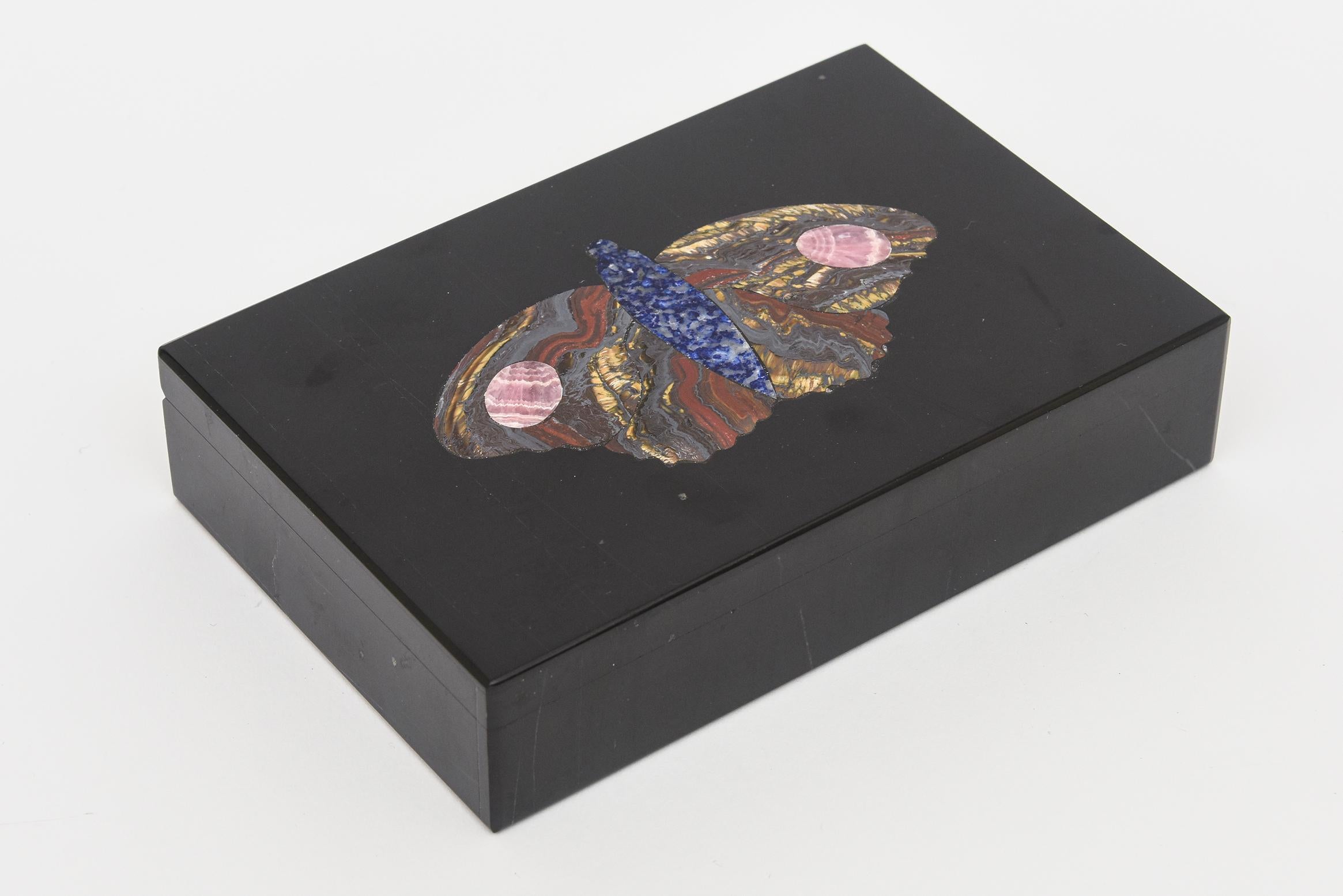 This stunning and hard to find vintage modernist Pietra Dura Italian stone hinged box has an elaborate butterfly in the center of the black marble. The sections of the butterfly have segmented lapis lazuli, tiger iron stone, pink rhodochrosite and a