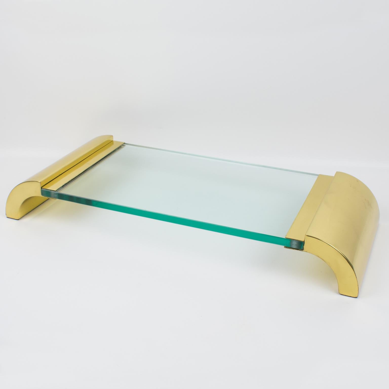 This lovely brass and glass pedestal centerpiece or display tray was designed in Italy in the 1980s. The serving piece has a modernist and minimalist design with massive polished brass raised sides, complemented with an extra thick glass slab. There