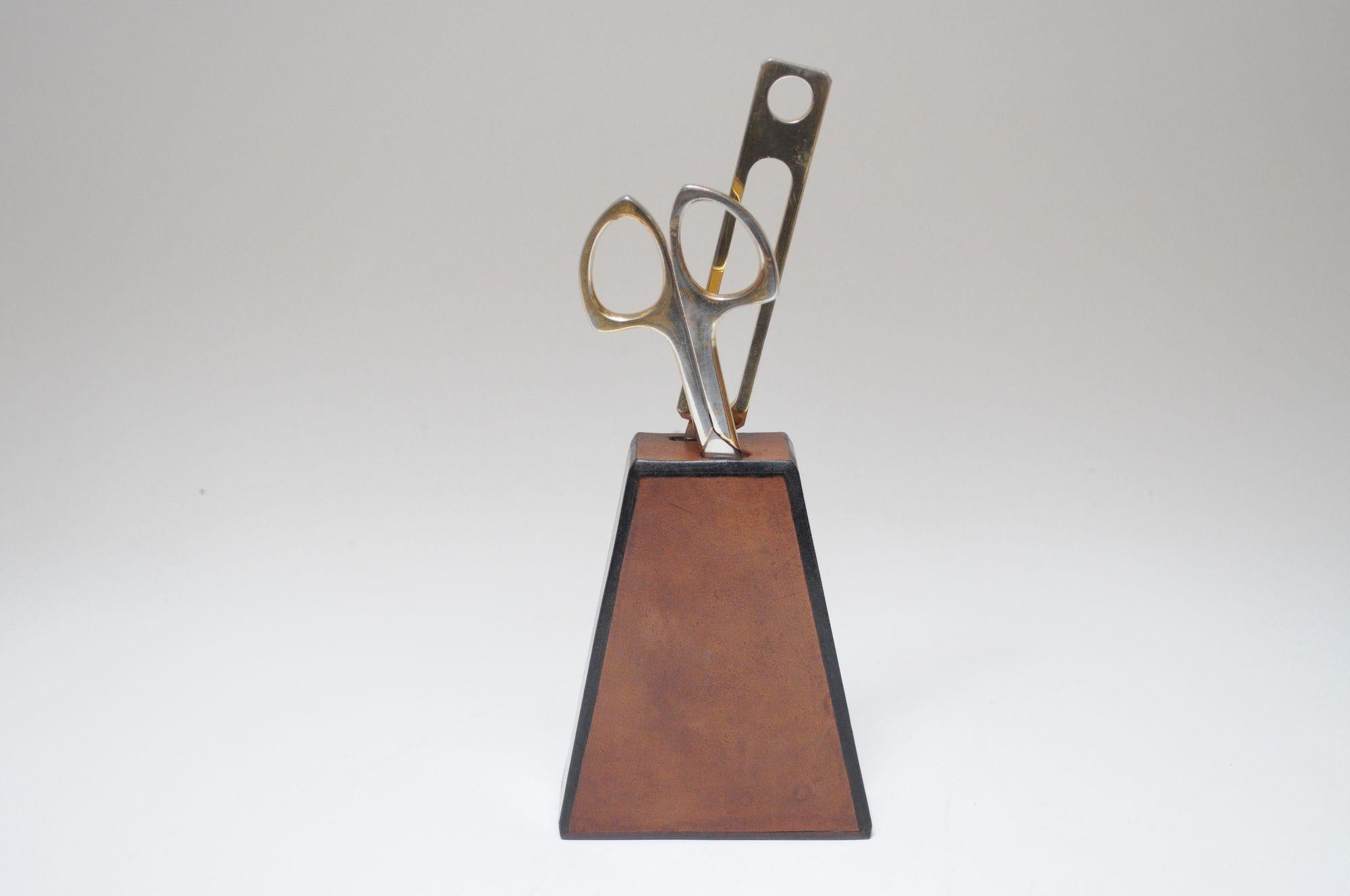 Juego vintage de tijeras y abrecartas chapados en latón dentro de un soporte de cuero (ca. 1960, Italia).
El acabado de latón se ha frotado en algunas partes por el envejecimiento natural, junto con el desgaste general, y el soporte de cuero muestra