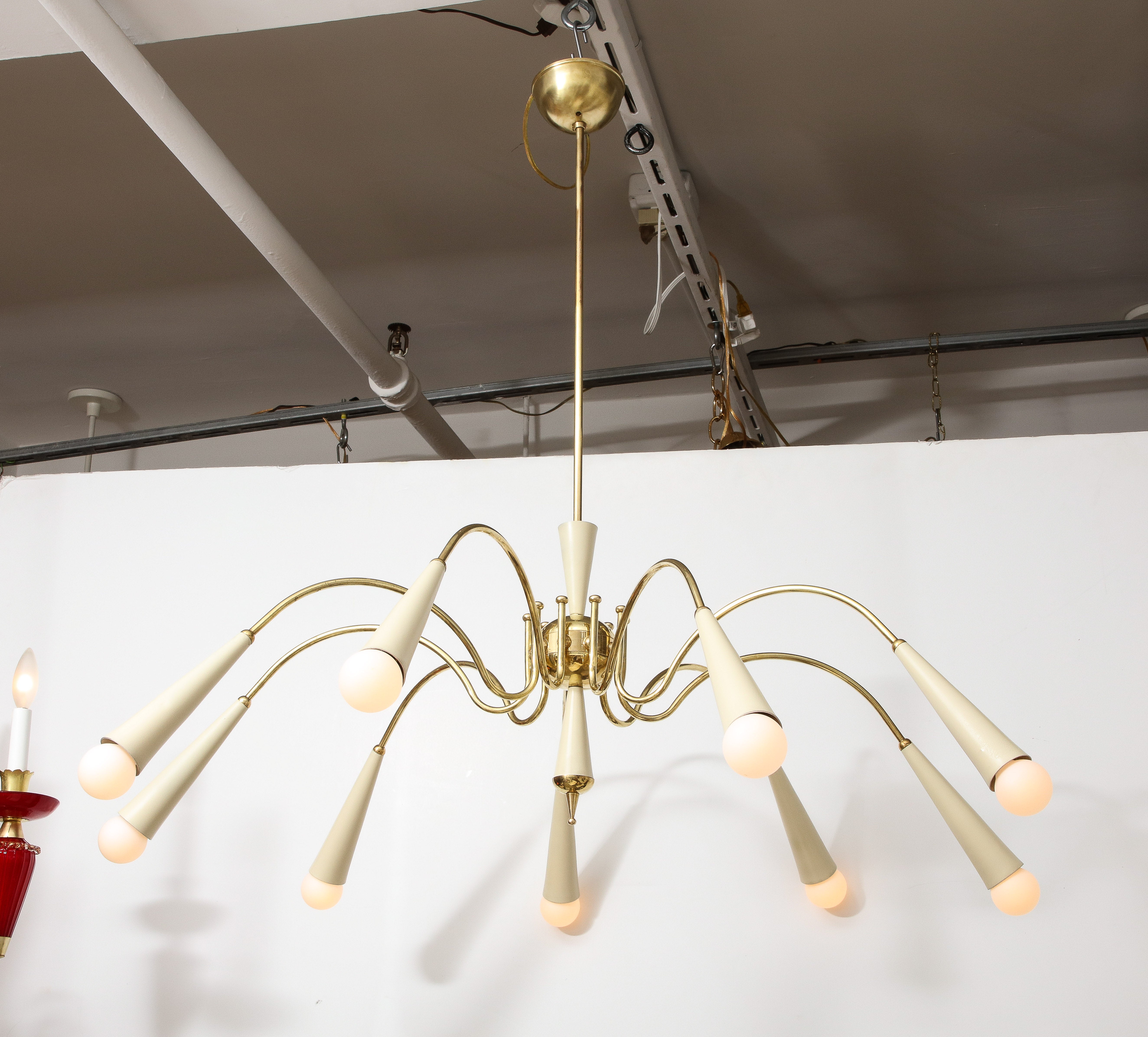 Italian modernist spider nine-arm chandelier in patinated brass and ivory white lacquer; the central brass fitting support the scrolled brass sweeping arms terminating with creamy lacquered enamel conical shaped bulb holders. With conical shaped