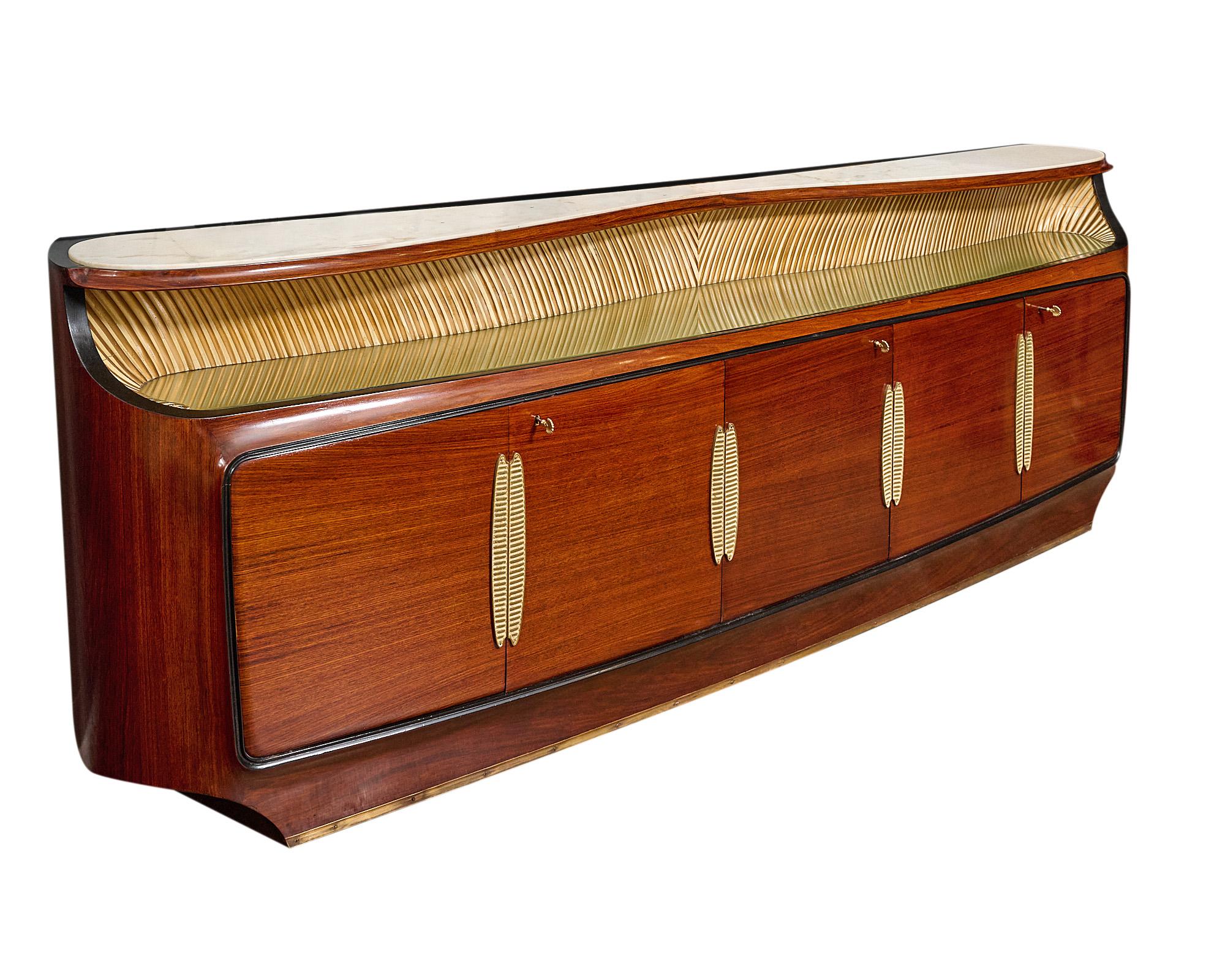 Grande buffet, credenza, Italian, of rosewood finished in a lustrous French polish, in the style of iconic designer Osvaldo Borsani, the rounded side board boasts five doors opening to ample storage and bar. Gilt brass hardware, working locks and