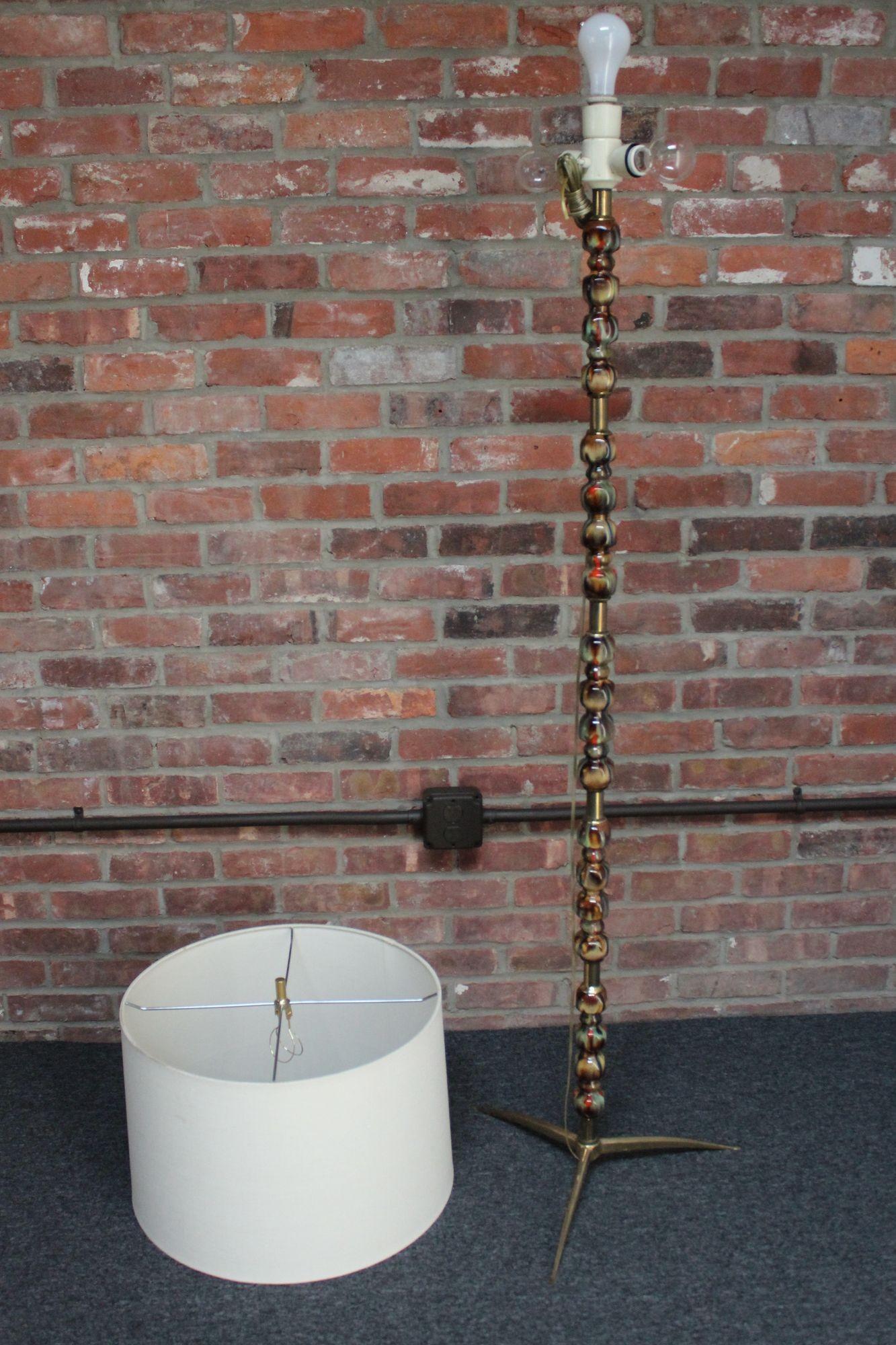 Italian floor lamp composed of clusters of sculptural ceramic adornments separated by brass brackets, all supported by a splayed tripod base (ca. 1960s).
Paired with an oversized, vintage drum shade, which shows light wear (one patch of