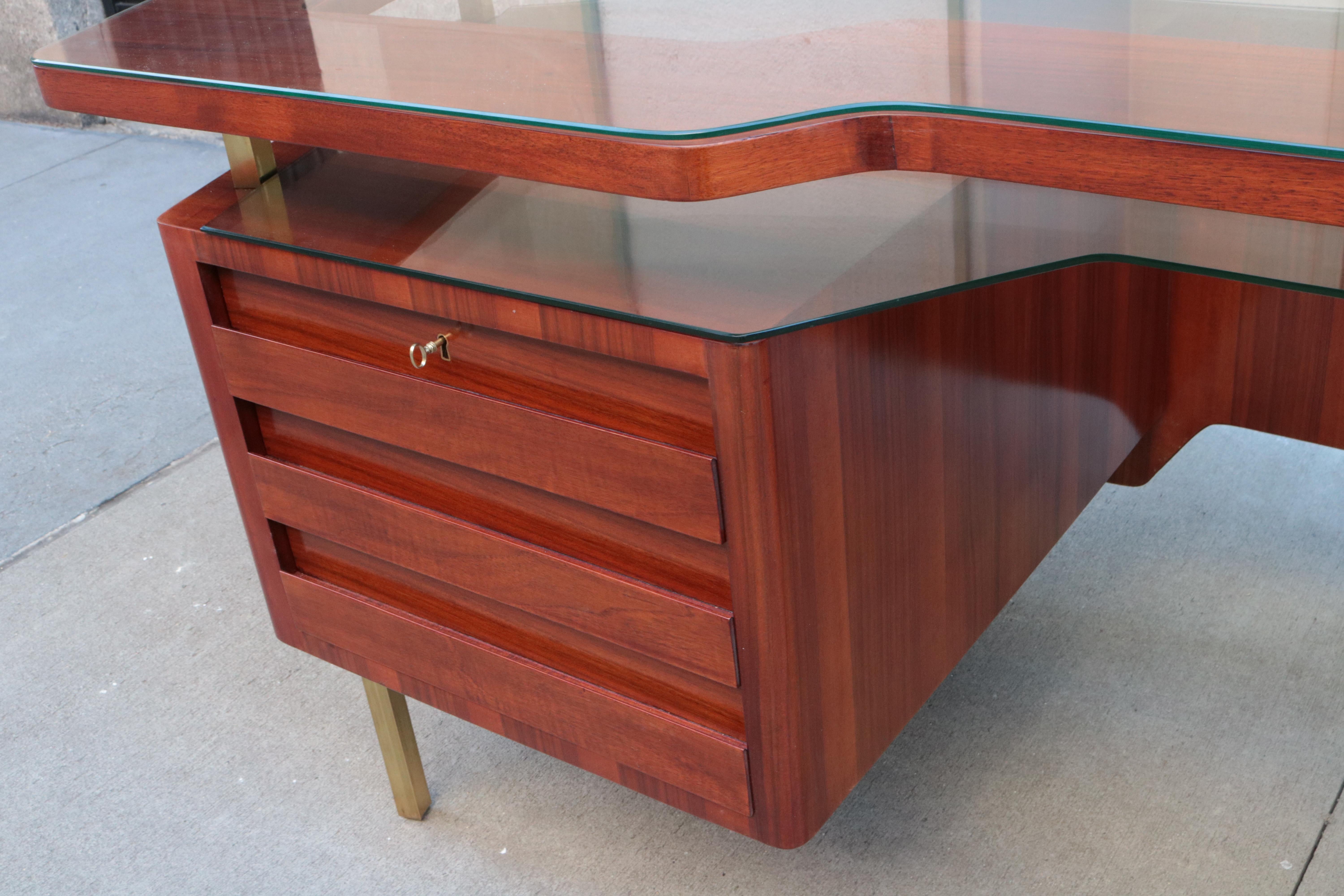 An Italian modernist desk.
Walnut with patinated brass legs,
a glass top and lower tier glass shelf.
 