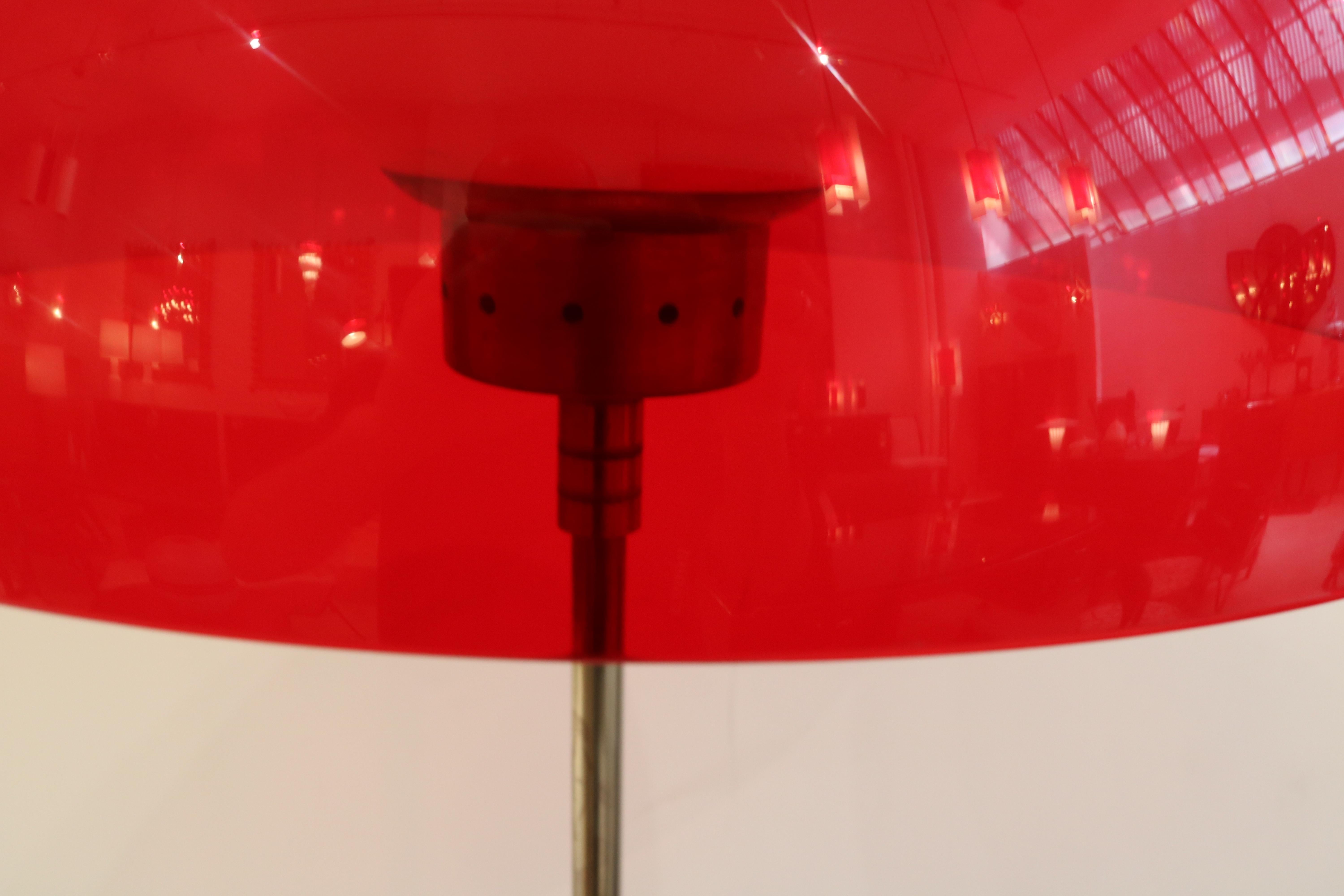 Italian Modernist floor lamp.
Red plastic shade merged with metal decorative elements and interior frosted glass globe.
Supported by patinated metal shaft resting on a marble base.