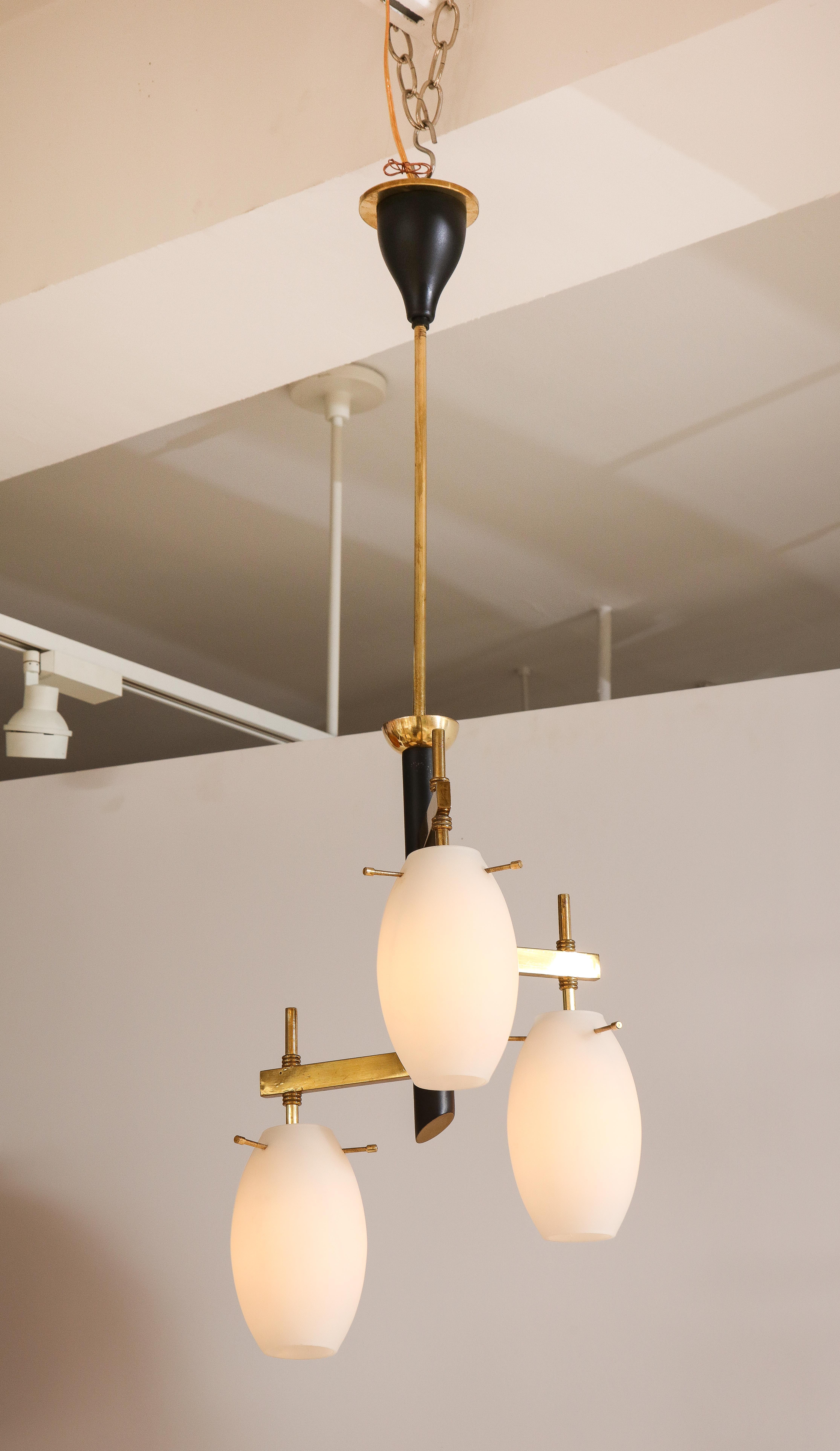 Un lustre moderniste italien avec trois ampoules en verre opalin qui s'étendent à partir de supports horizontaux en laiton. La tige en métal noir et laiton, avec son baldaquin original en métal noir et laiton en forme de tulipe. Nouvellement recâblé