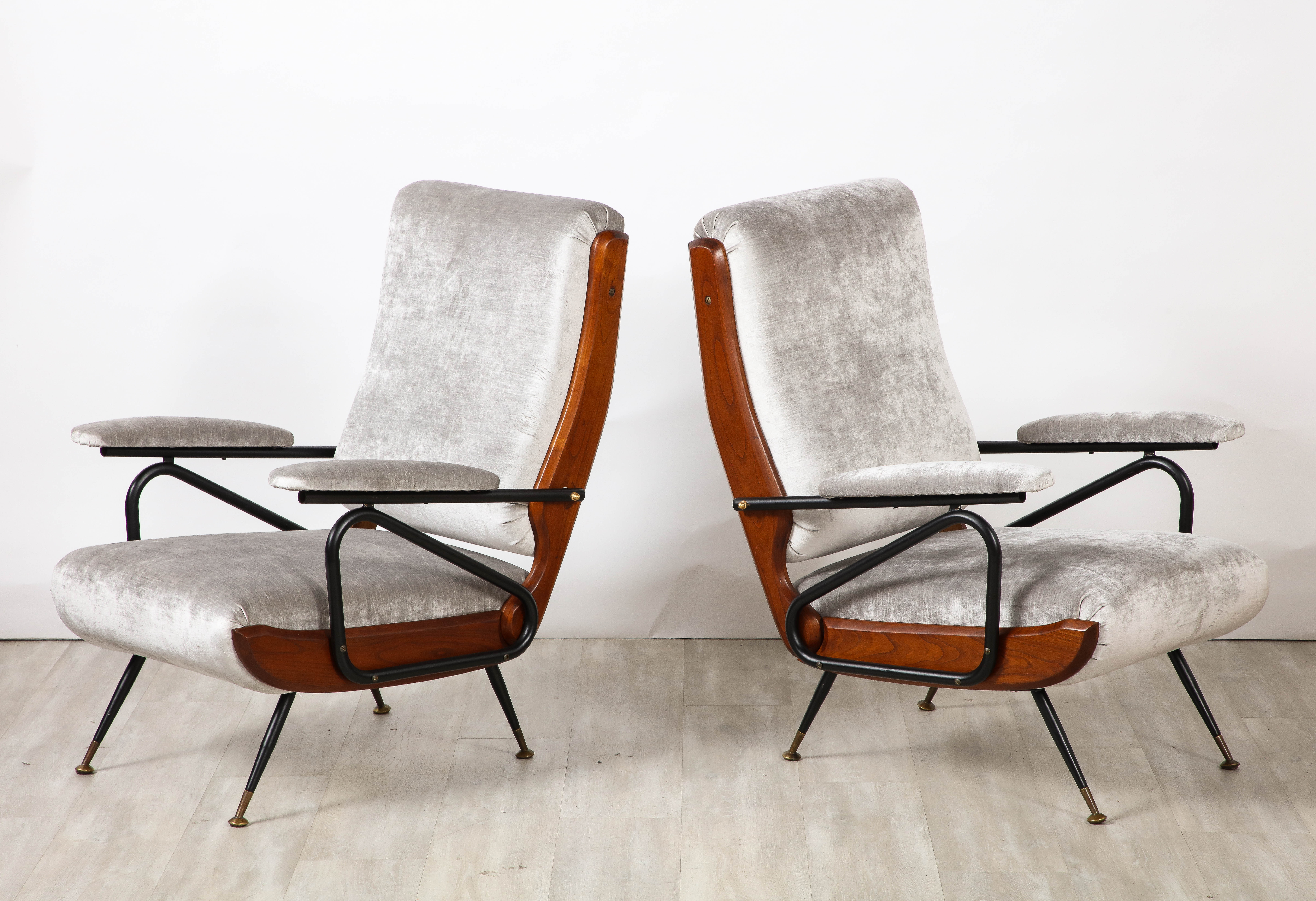 A pair of Italian modernist reclining lounge chairs / arm chairs, the geometric metal frames accentuate the molded walnut surround on the sides of the back and seats, the legs tapered metal ending in brass sabot.  Newly upholster in a neutral grey