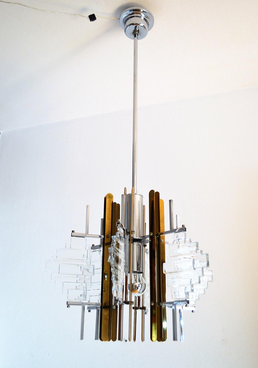 Beautiful chandelier typical for the Italian modernist era, designed by Gaetano Sciolari.
The chandelier is made of shiny chrome plated and dark brass parts as well as 5 glass parts in architectonic design in the form of a star made of 5 arms