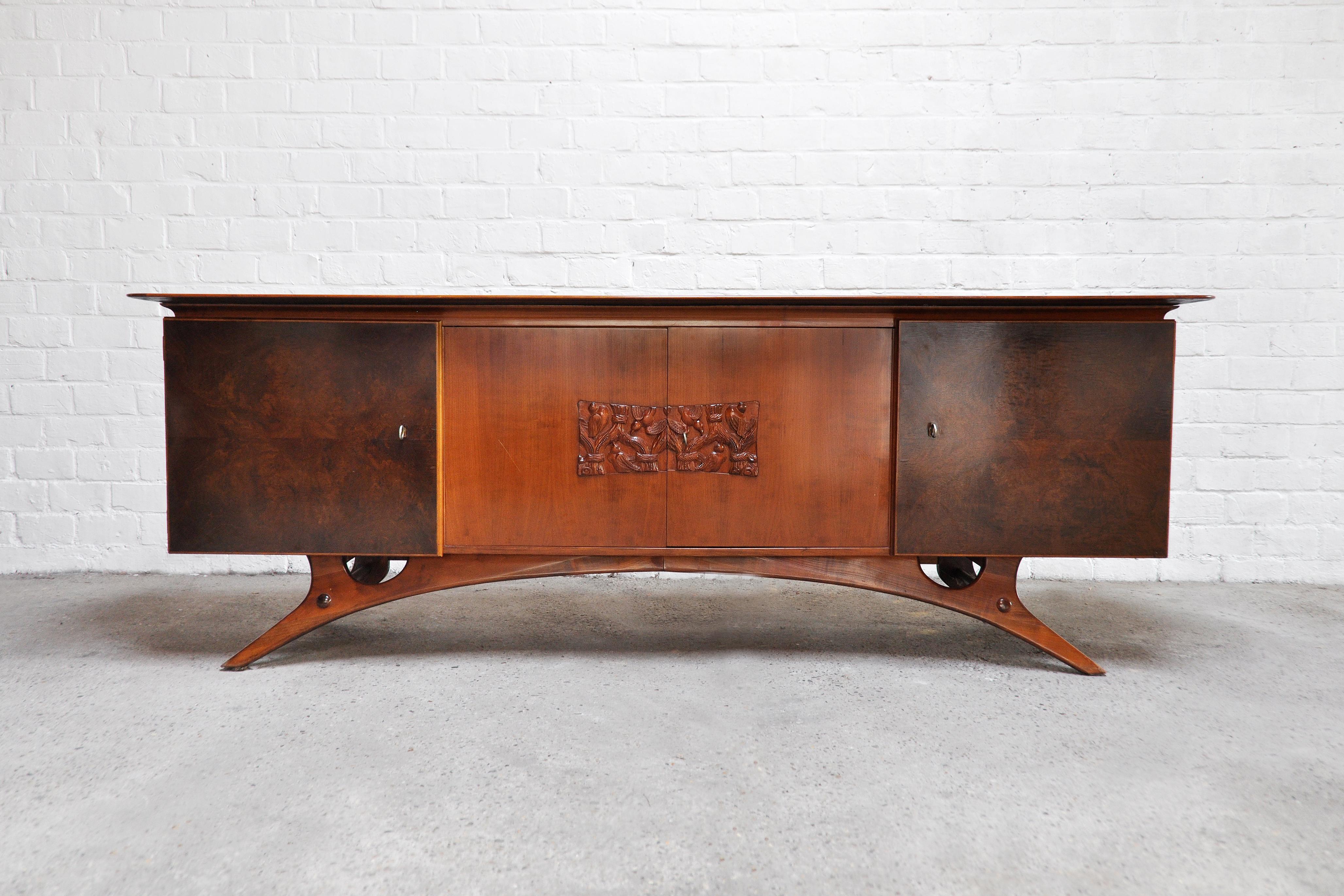 A fabulous Italian sideboard with a unique sculptural base and a modernist bas-relief carving depicting songbirds. Constructed out of mixed woods such as teak, veneer and walnut. Features four dours including the original keys. The designer is