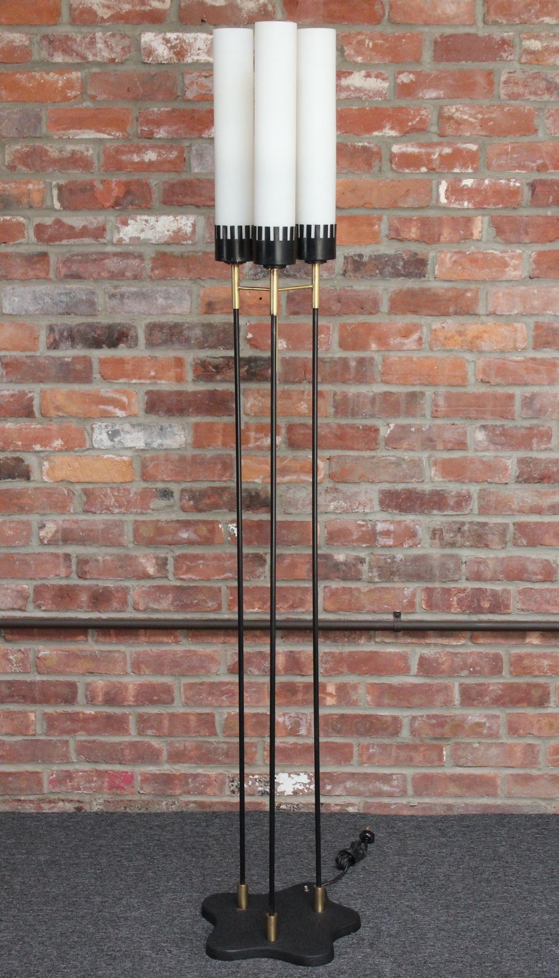 Triple socket floor lamp composed of black enameled-metal stems and steel base with brass accents and cased glass cylindrical fixtures by Stilnovo (Italy, ca. 1950s).
The three sockets are housed within cut metal 'receptacles' resembling