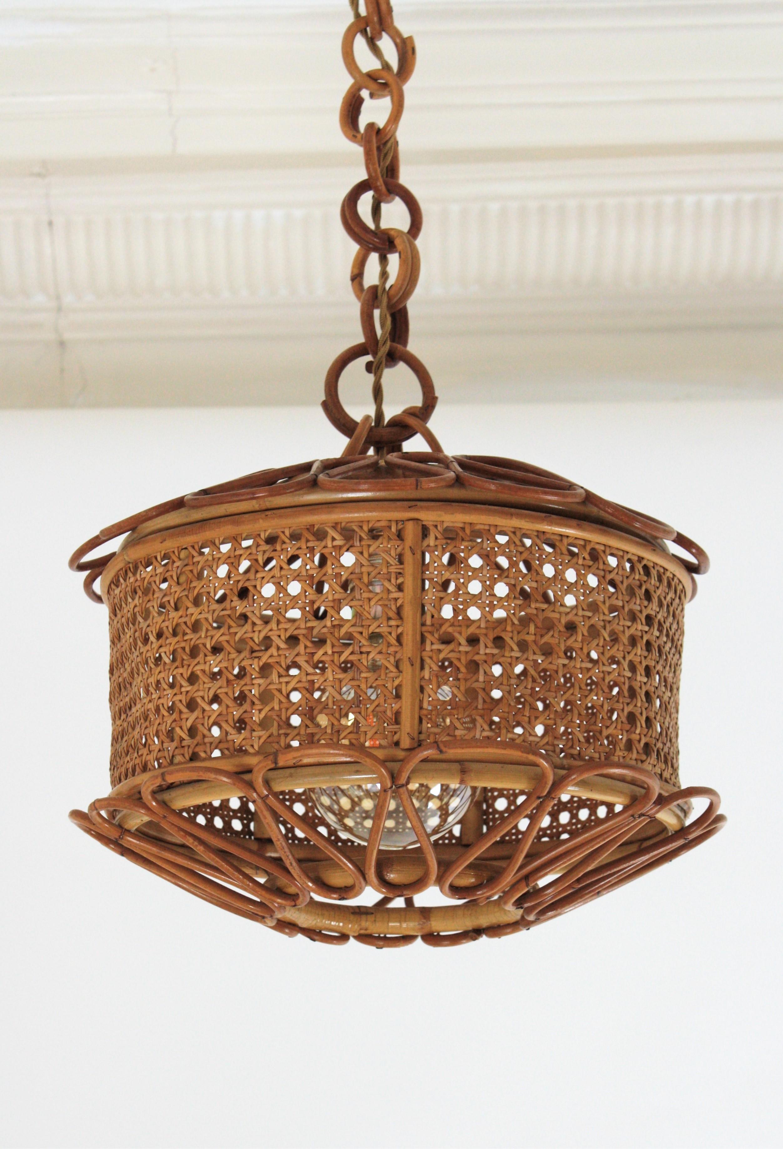 Beautiful Mid-Century Modern woven wicker wire and rattan pendant lamp / lantern, Italy, 1950s.
The woven wicker cylindrical shade of this lamp is accented by handcrafted rattan details as petals at the bottom and at the top. It hangs from a chain