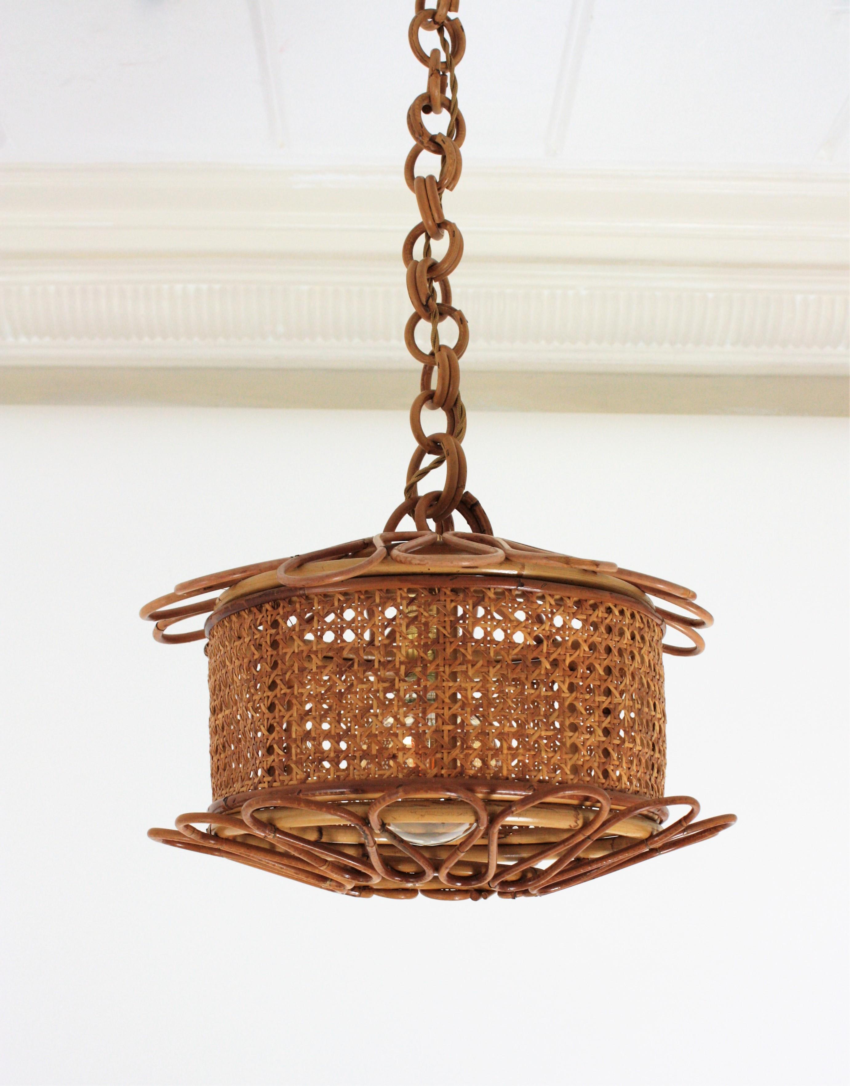 Beautiful Mid-Century Modern woven wicker wire and rattan pendant lamp / lantern, Italy, 1950s.
The woven wicker cylindrical shade of this lamp is accented by handcrafted rattan details as petals at the bottom and at the top. It hangs from a chain