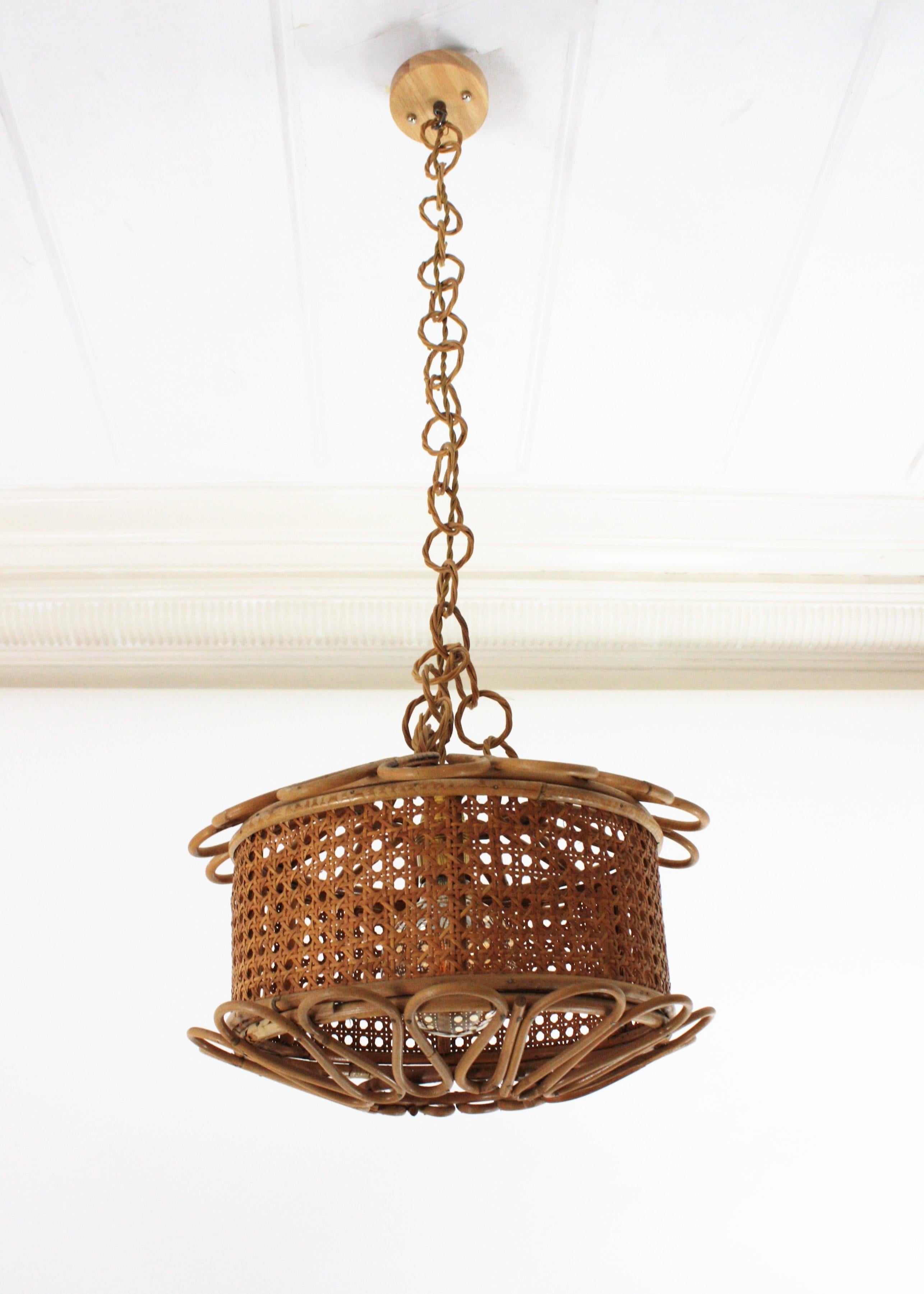 Beautiful Mid-Century Modern woven wicker wire and rattan pendant lamp / lantern, Italy, 1950s.
The woven wicker cylindrical shade of this lamp is accented by handcrafted rattan details as petals at the bottom and at the top. It hangs from a chain