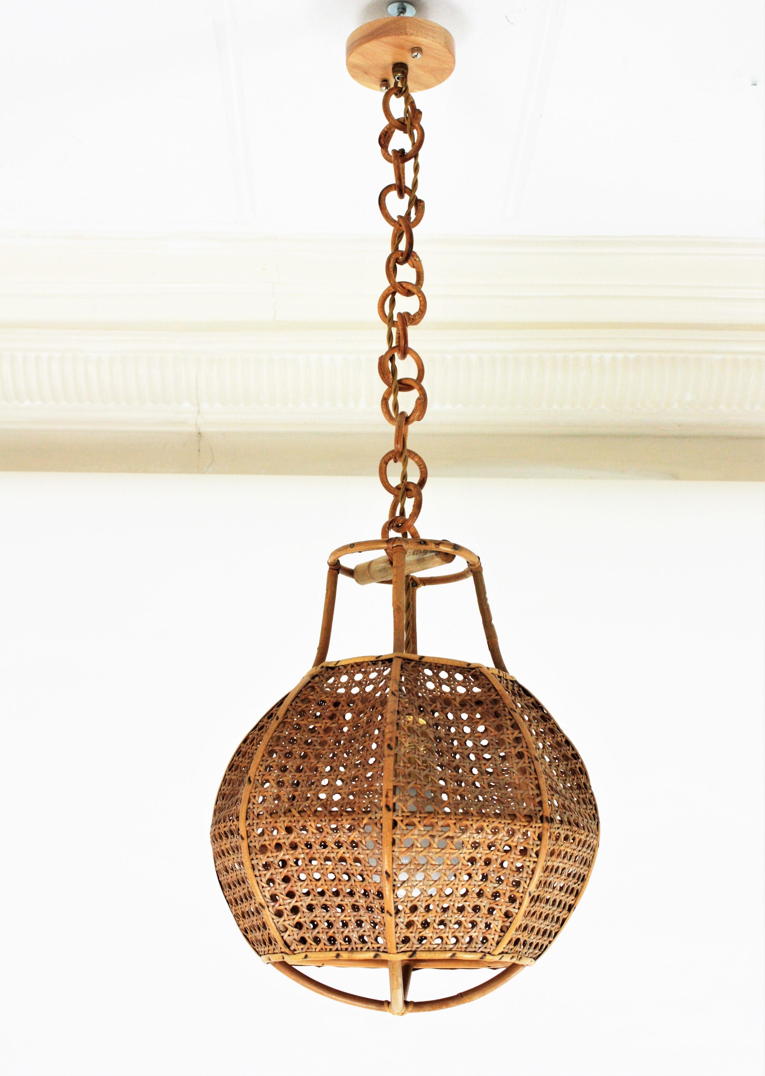 Mid-Century Modern woven wicker wire and rattan globe shaped lantern or pendant ceiling lamp, Italy, 1950s. 
The woven wicker spherical shade of this lamp is accented by rattan details. It hangs from a chain with round rattan links that can be cut