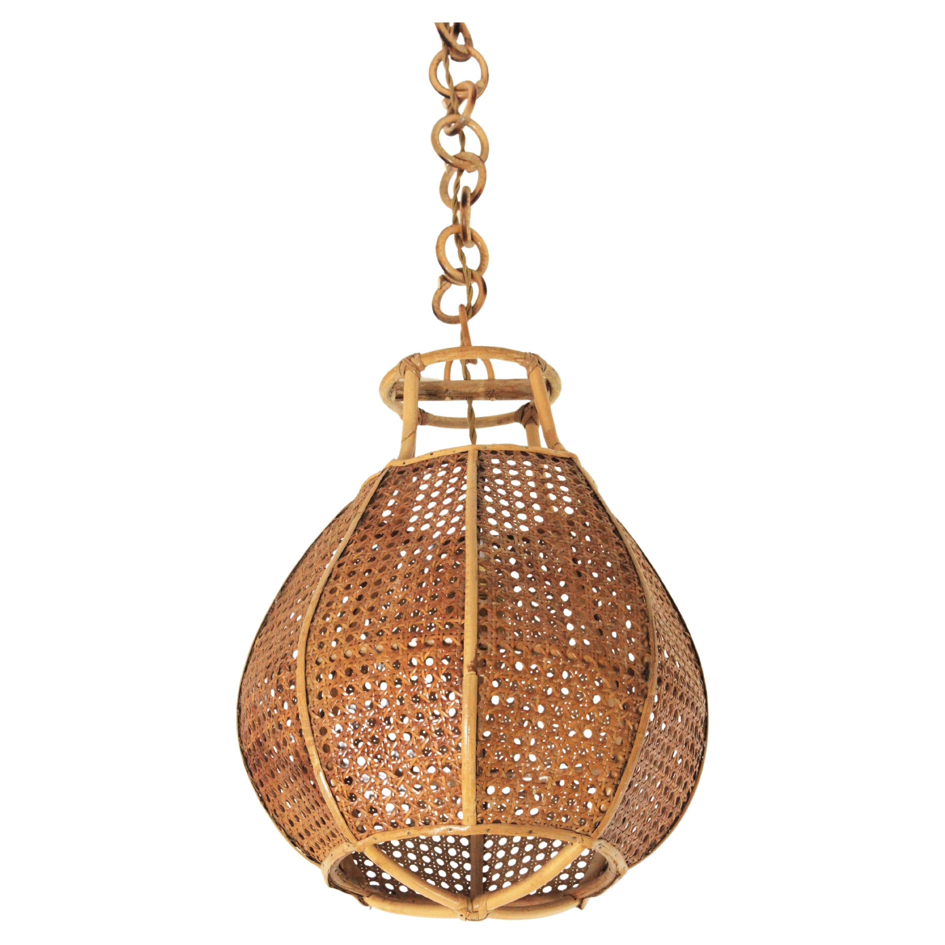 Mid-Century Modern woven wicker and rattan globe shaped lantern or pendant ceiling lamp. Italy, 1950s-1960s.
The woven wicker spherical shade of this lamp is accented by rattan details. It hangs from a chain with round rattan links that can be cut