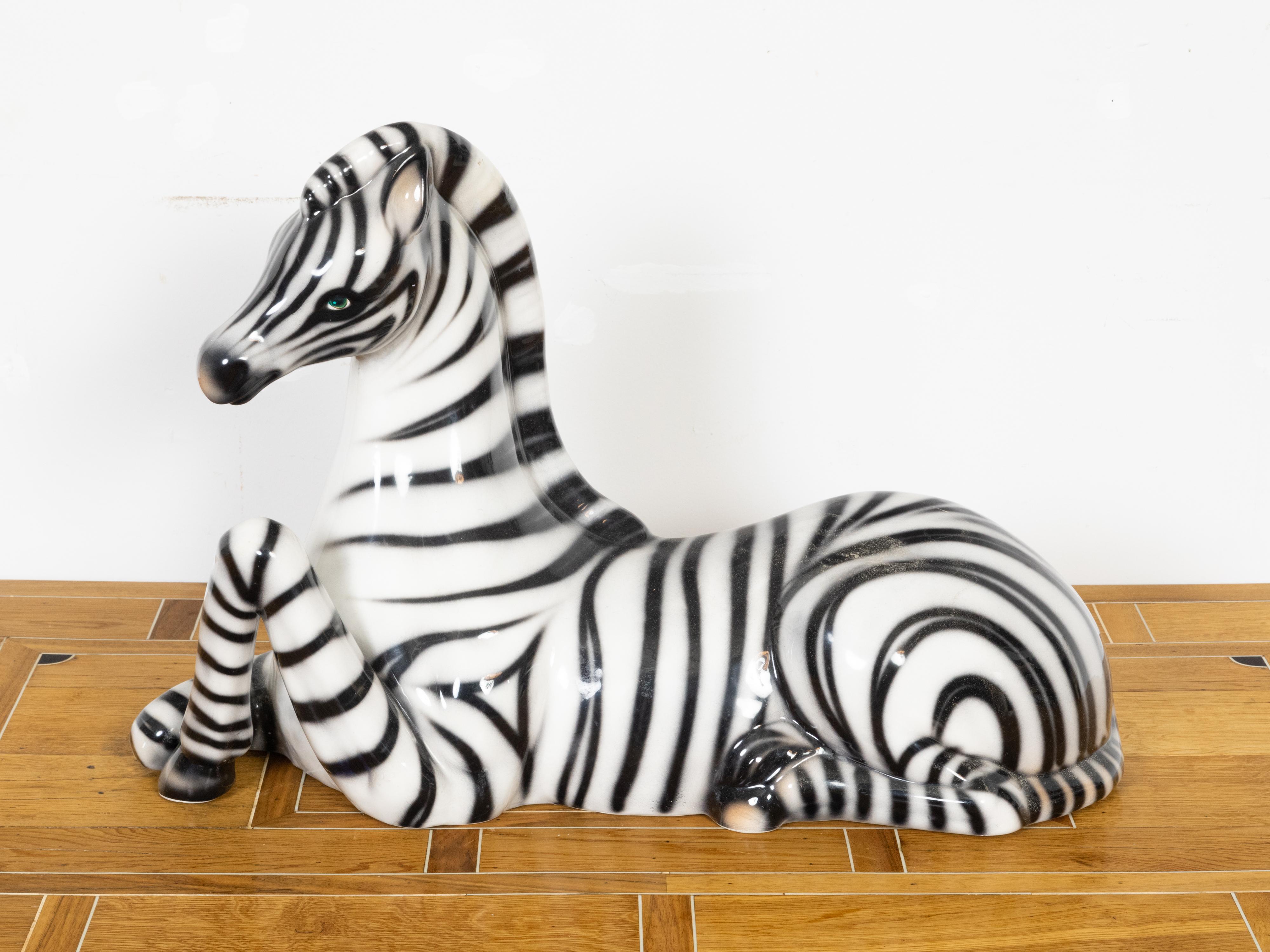 A vintage Italian glass animal sculpture depicting a zebra lying on the ground, with green eyes and embossed mark. Created in Italy during the Midcentury period, this glass sculpture charms us with its delicate depiction of a zebra peacefully