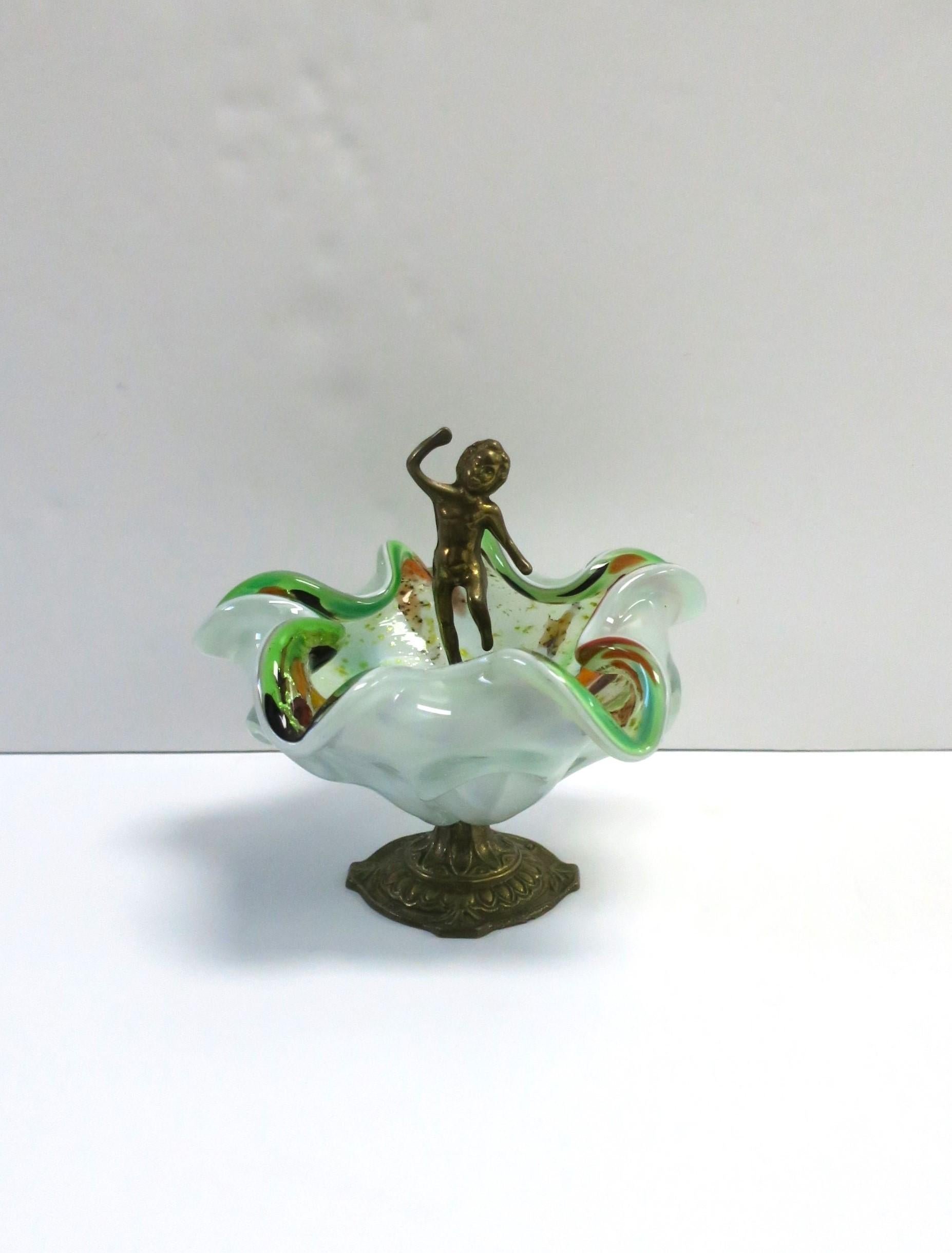 An Italian Murano art glass bowl with brass nude male figure, circa mid-20th century, Italy. This Murano bowl has a wavey soft edge with bright green and orange hues, hints of gold, brown and light blue splashes of art glass. A brass nude male