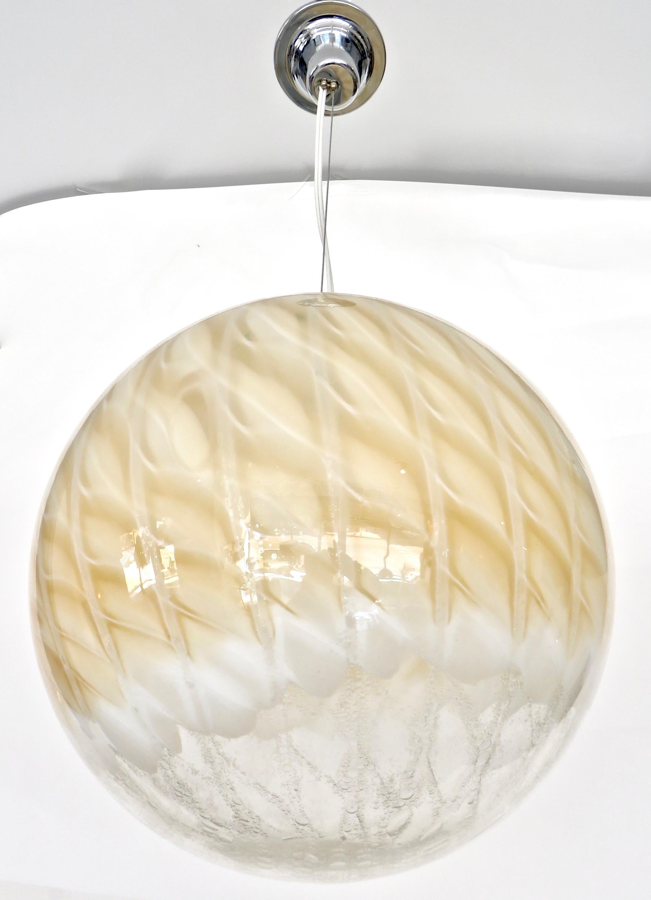 A large blown Murano glass globe attributed to Italian glass maker Venini.
Pale champagne to crème caramel color swirls of color with small bubbles in the glass.
The length of the handing wire and cord can be lengthened or shortened to