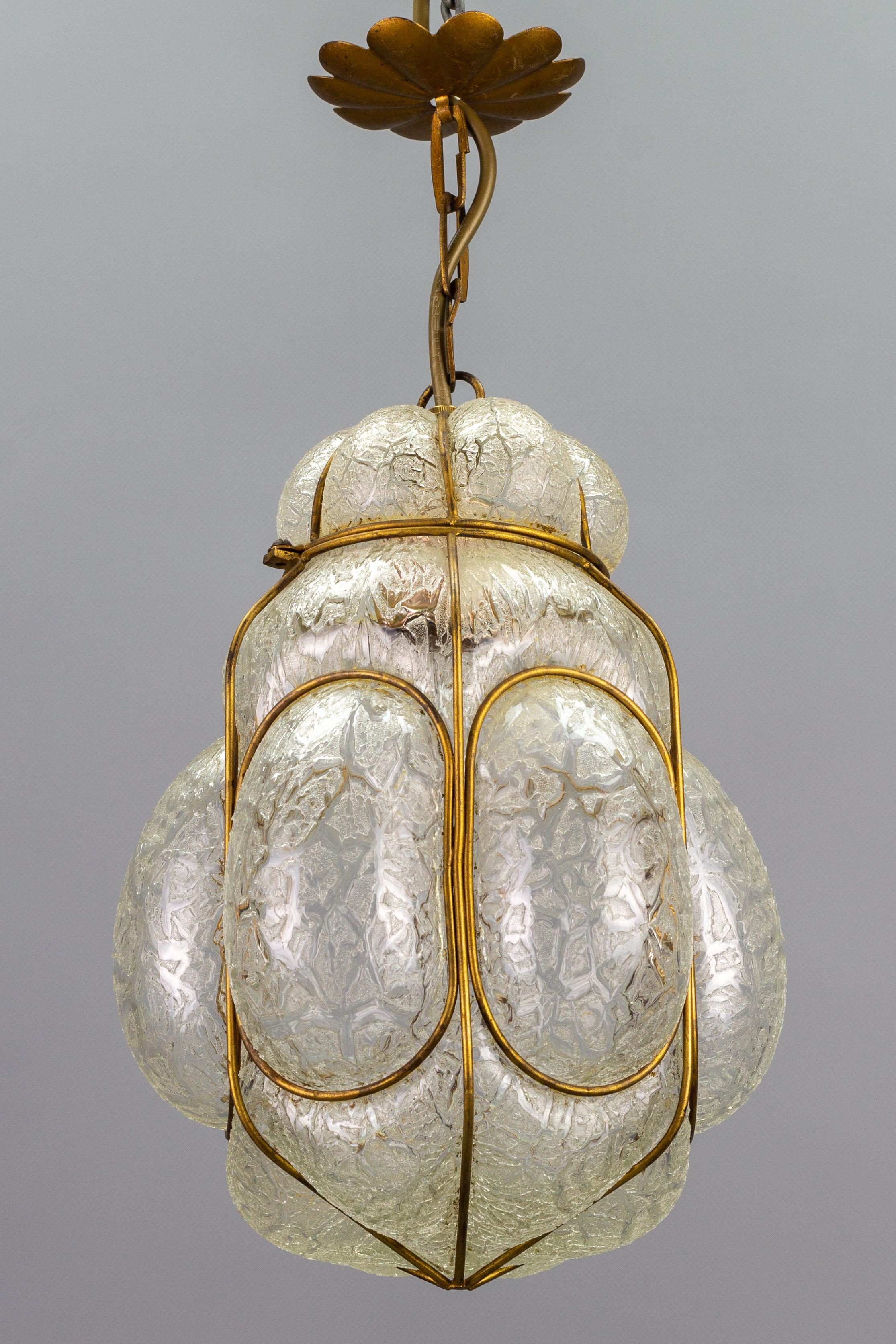 This beautiful Murano Seguso style Venetian pendant lamp or lantern features hand-blown granite texture glass in frosted white and clear tones with a decorative golden iron cage.
One socket for E27 (E26) size light bulb.
Dimensions: Height: 40 cm