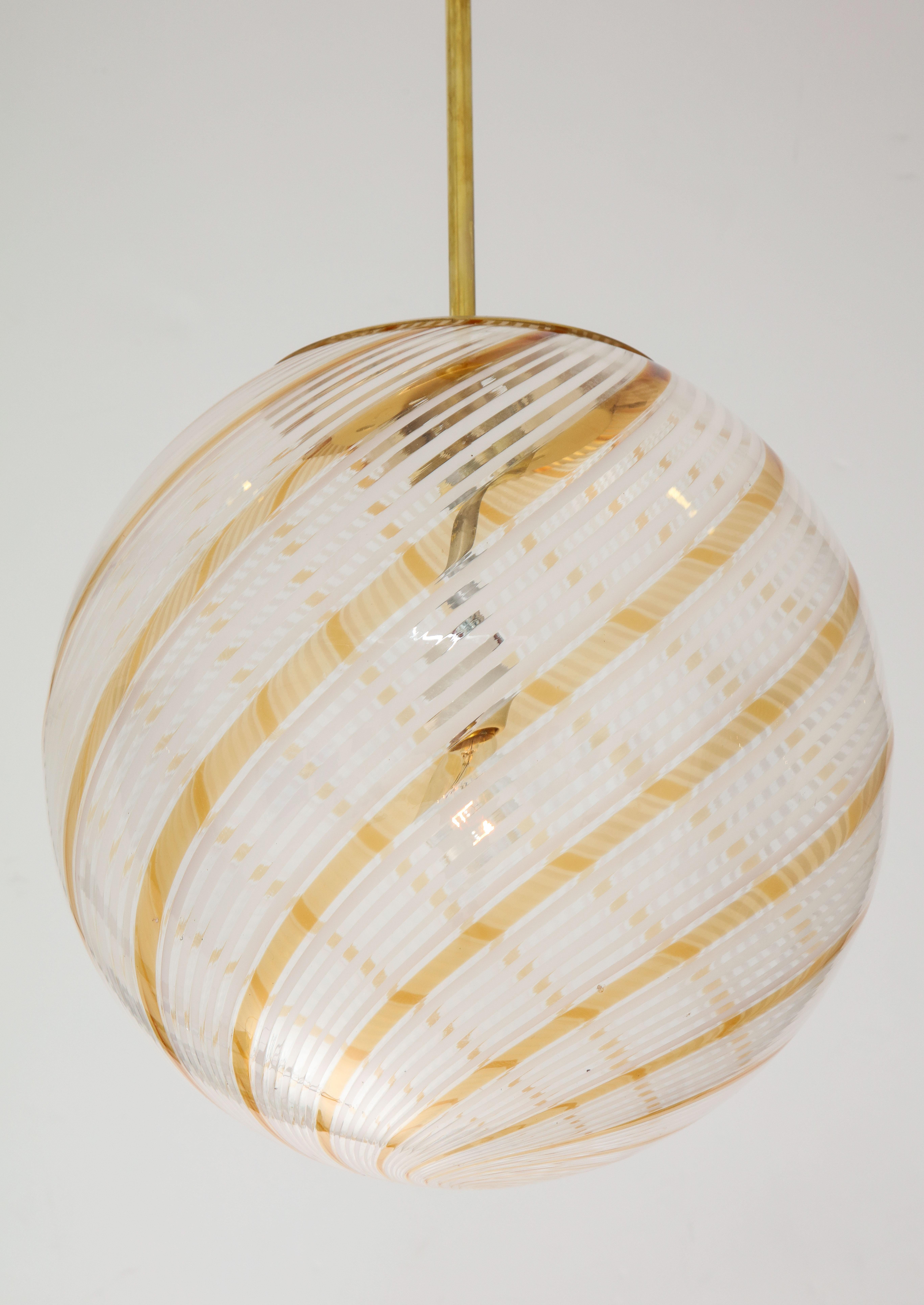 An Italian mid century handblown Murano chandelier or pendant designed by Lino Tagliapietra for La Murrina, Venice, circa 1970. The glass globe comprised of broad spirals of an alternating gold and white design suspended on a brass pole with