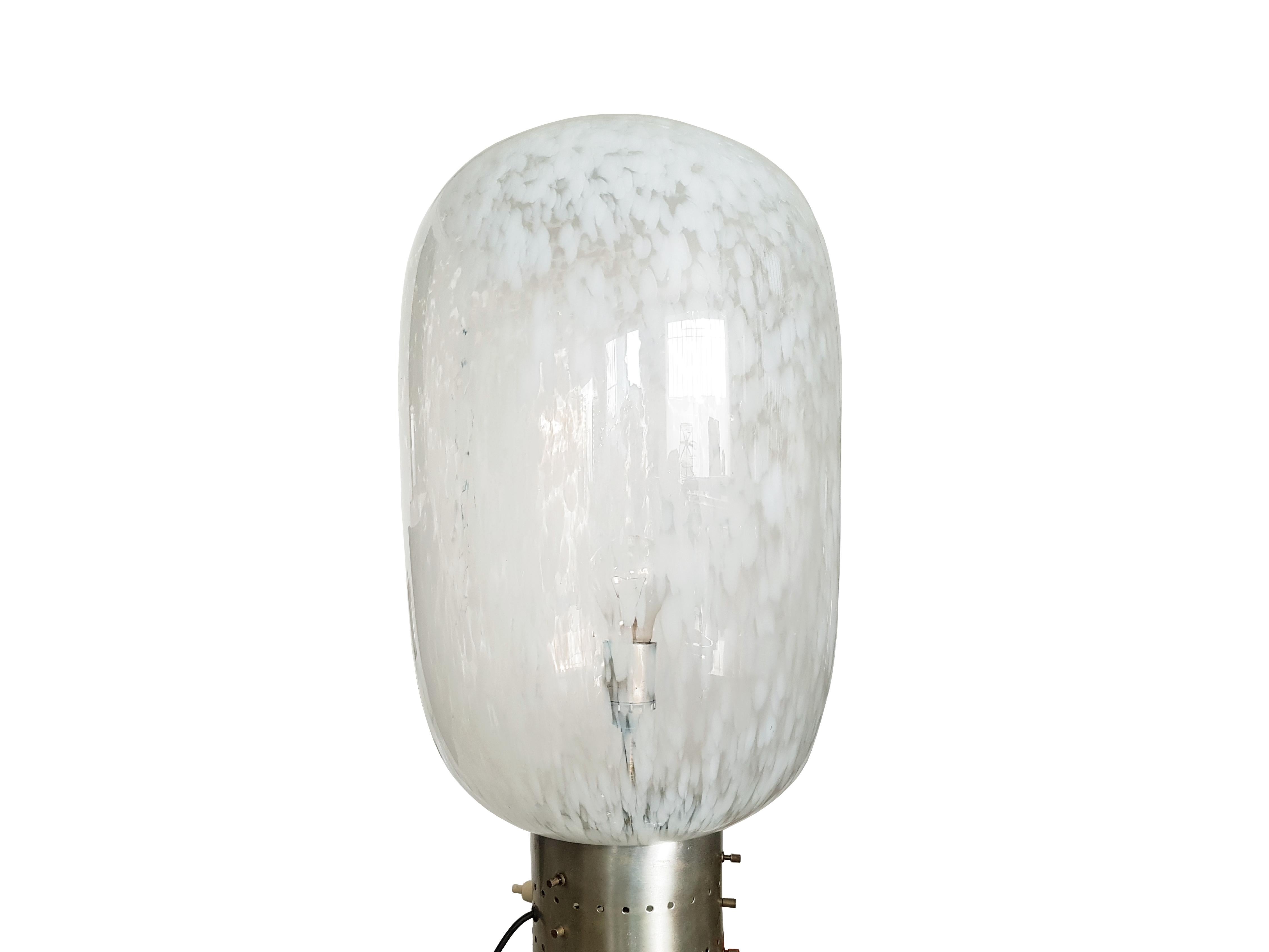 Diese schöne Stehlampe wurde um 1960 in Italien hergestellt. Sie besteht aus 2 handgefertigten Muranoglasschirmen, die durch einen zylindrischen Metallgürtel miteinander verbunden sind.
Die Leuchte verfügt über 2 E27-Glühbirnenfassungen, die