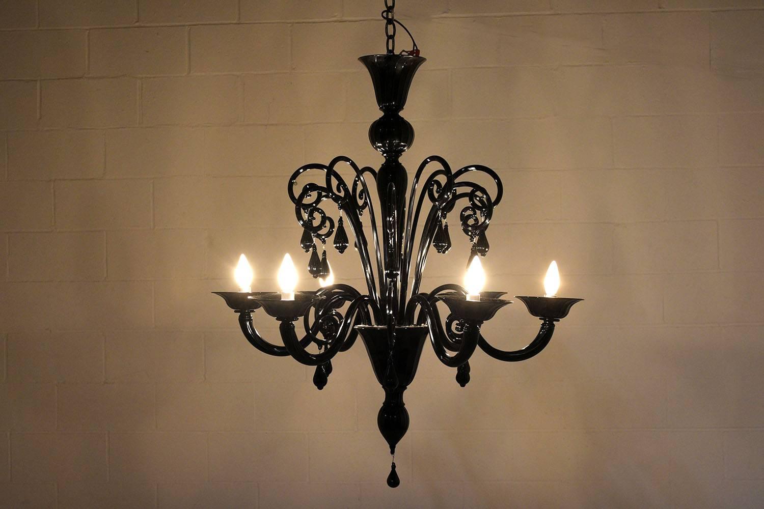 This Vintage Italian Six-Arm Chandelier features a Murano glass body finished in a striking black color and the glass is accented with fluted details. The piece features blow glass shaped into scrolls with curved arms and hanging from the top,
