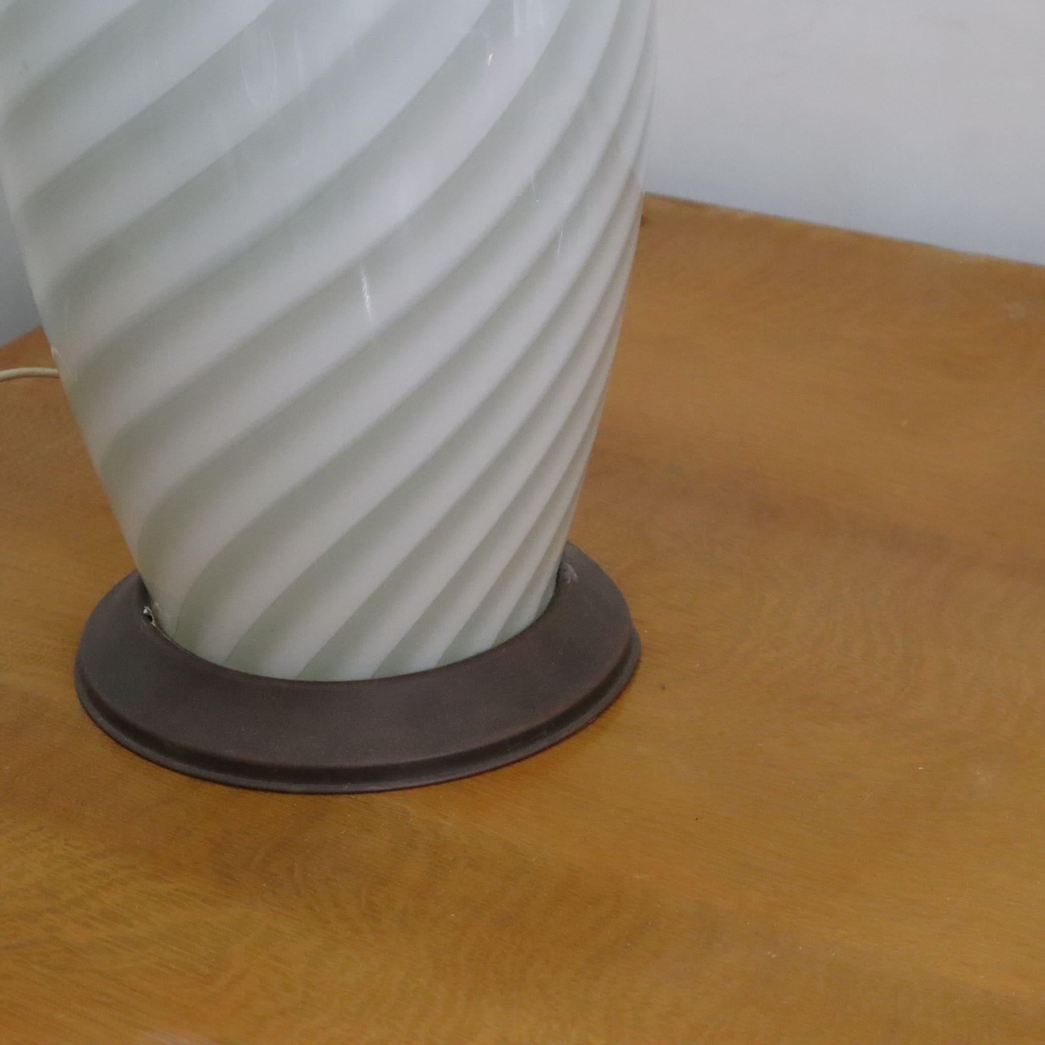 The Murano glass and brass table lamp by Tommaso Barbi, made in the 70s, is a refined example of vintage Italian design. This piece combines the timeless elegance of Murano glass with the strength and shine of brass, distinctive characteristics of