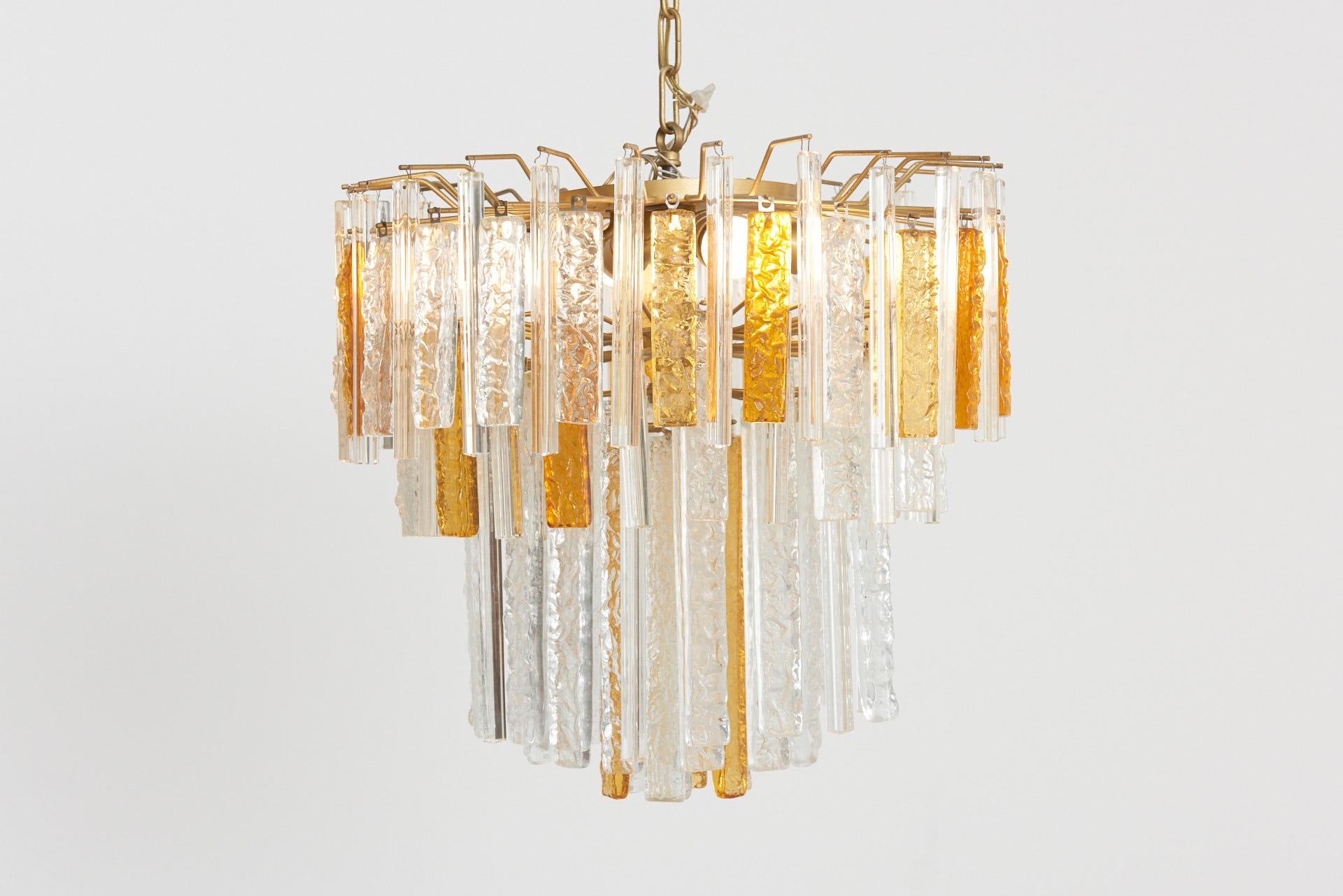 Italian chandelier from the 1960s, designed by Toni Zuccheri and made by Venini. Handmade Murano glass pieces with different lengths, cross section, texture and color alternate one another. The brass structure with four lamps bears the glass pieces