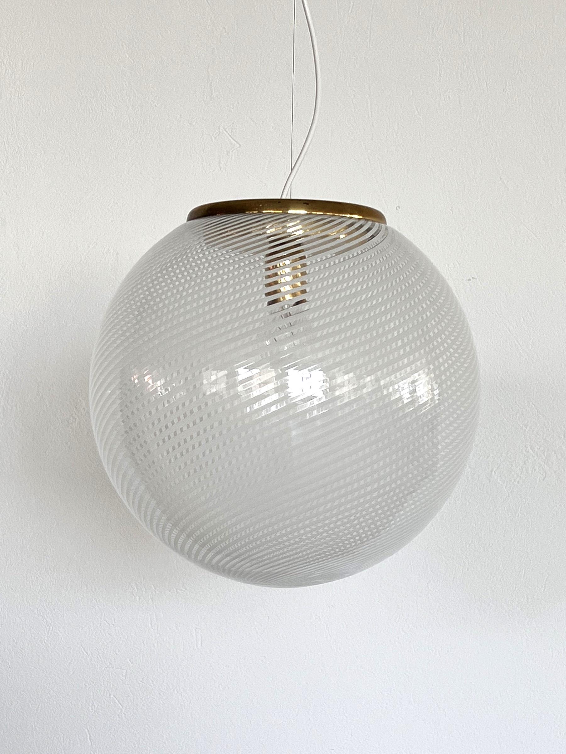 Gorgeous pendant light with large murano glass globe and brass detail.
Made in Italy in the 1970s.
The beautiful glass globe presents shiny white stripes on transparent glass ground. 
When illuminated, leaves gorgeous shadows on the near wall /