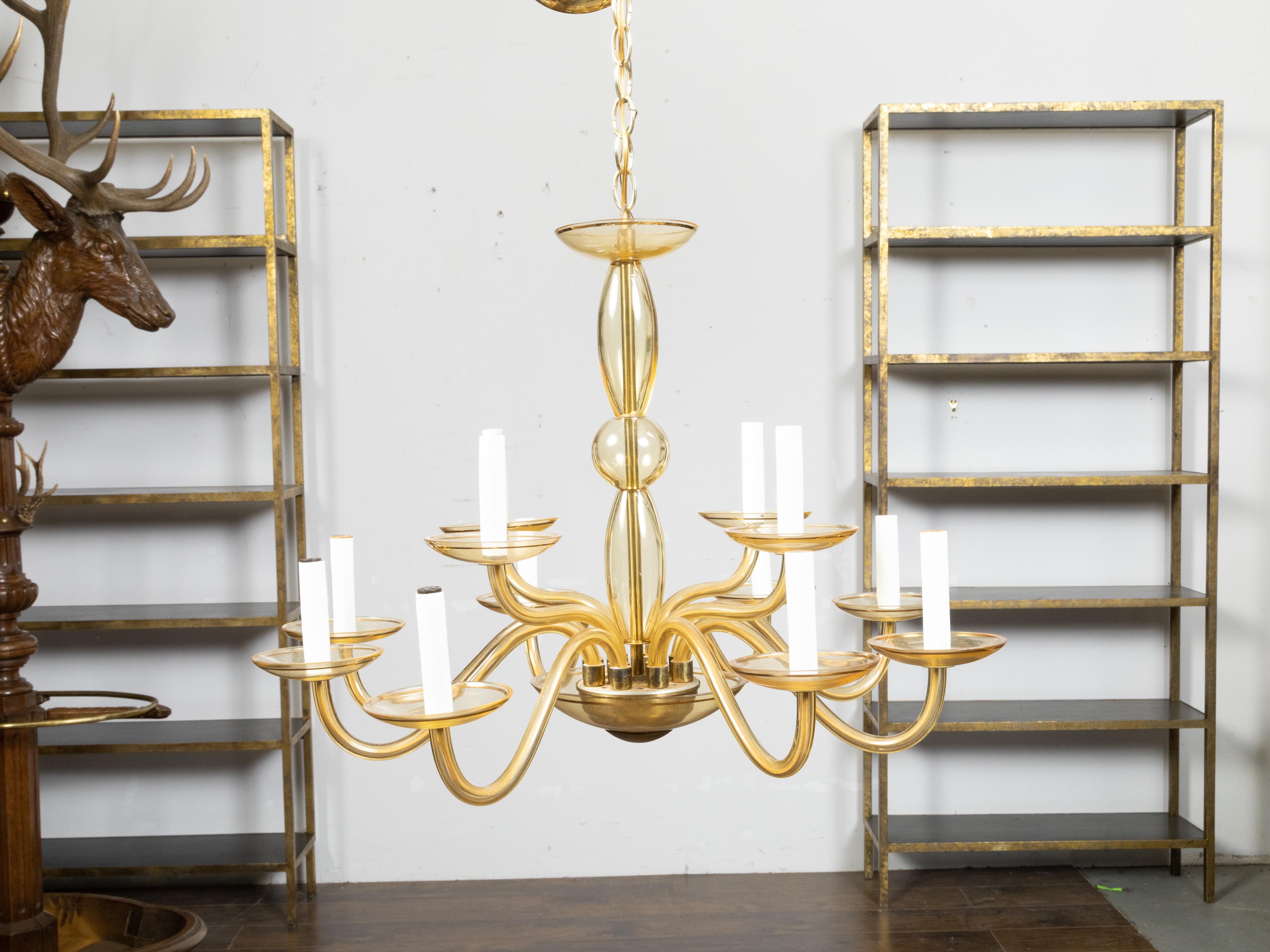An Italian Murano glass chandelier from the mid 20th century with 12 lights and golden tones. Created on the island of Murano in Italy during the Midcentury period, this hand-blown glass chandelier features a central column connected to a lower