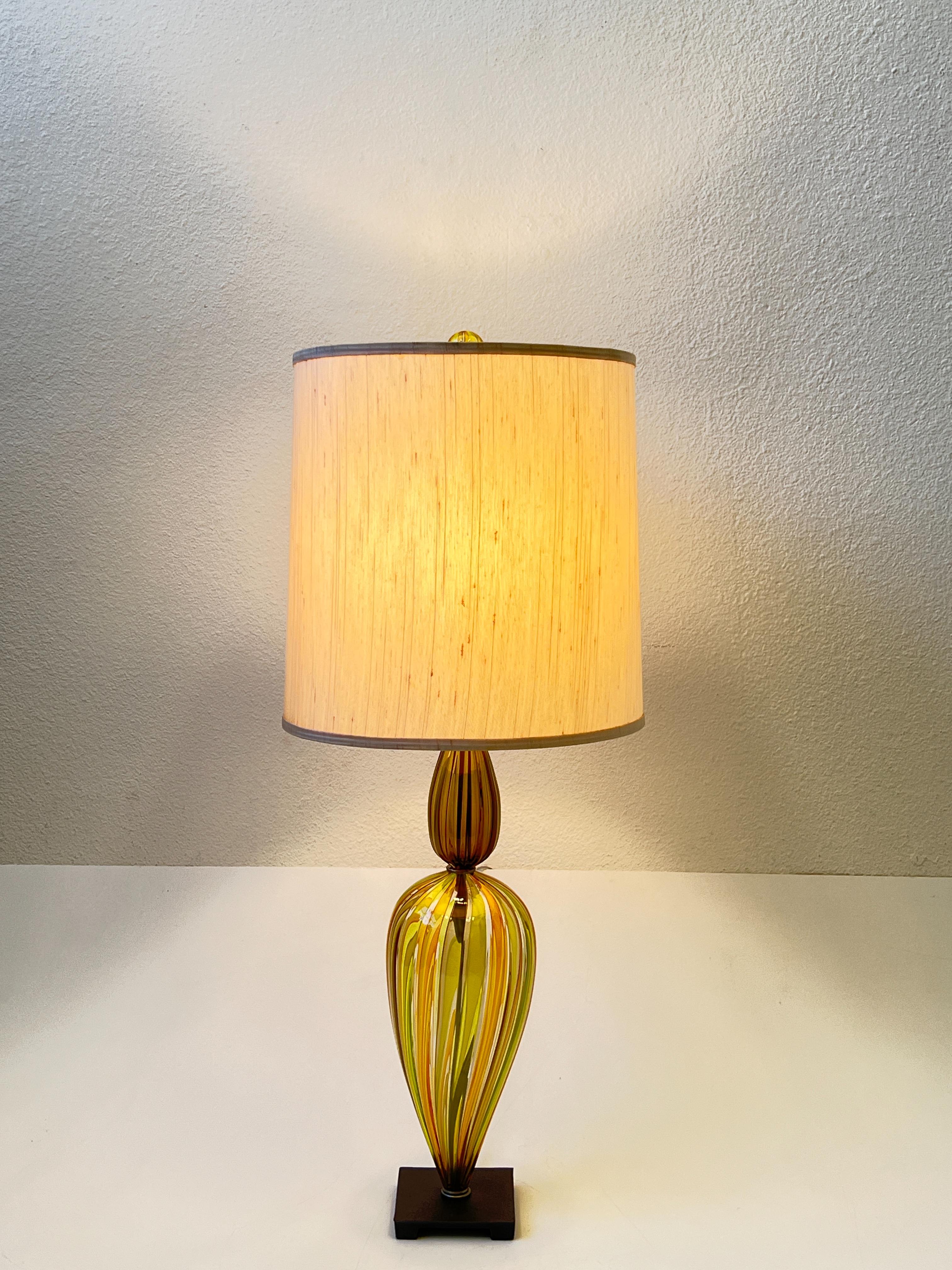 Magnifique lampe de table en verre Murano de Venini datant des années 1960. 
La partie inférieure de la lampe et le fleuron sont en verre de Murano à rayures jaunes et vertes, la partie supérieure est en verre de Murano fumé, avec des ferrures en