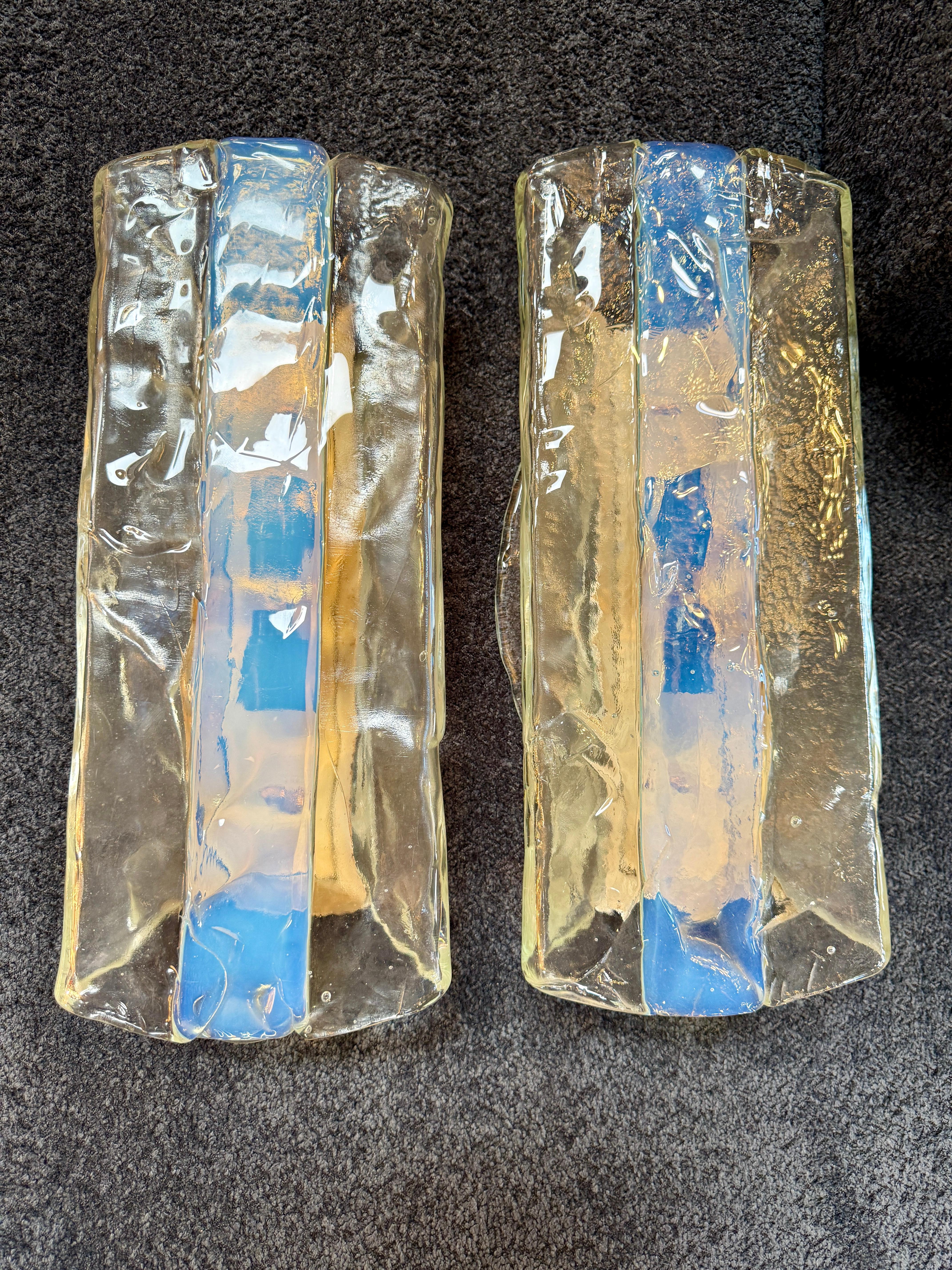 A luminous trio of sculptural sconces by Mazzega, expertly crafted from Murano glass in Italy during the late 1960s to early 1970s. Each piece showcases a bold, organic form in thick, hand-pulled glass, combining clear and opalescent bands with a
