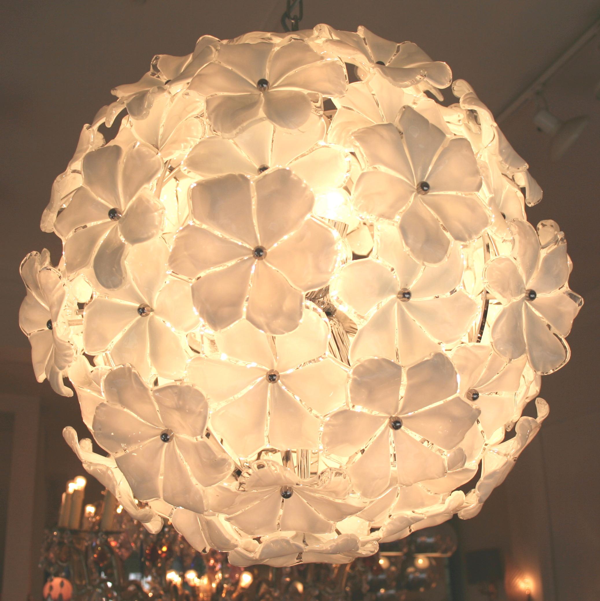 Superbe lustre contemporain en forme de globe de Murano. Chaque fleur opaque et blanche est réalisée en verre de Murano soufflé à la main et fixée sur le cadre par une petite tige circulaire en chrome.
Disponible avec un cadre doré ou