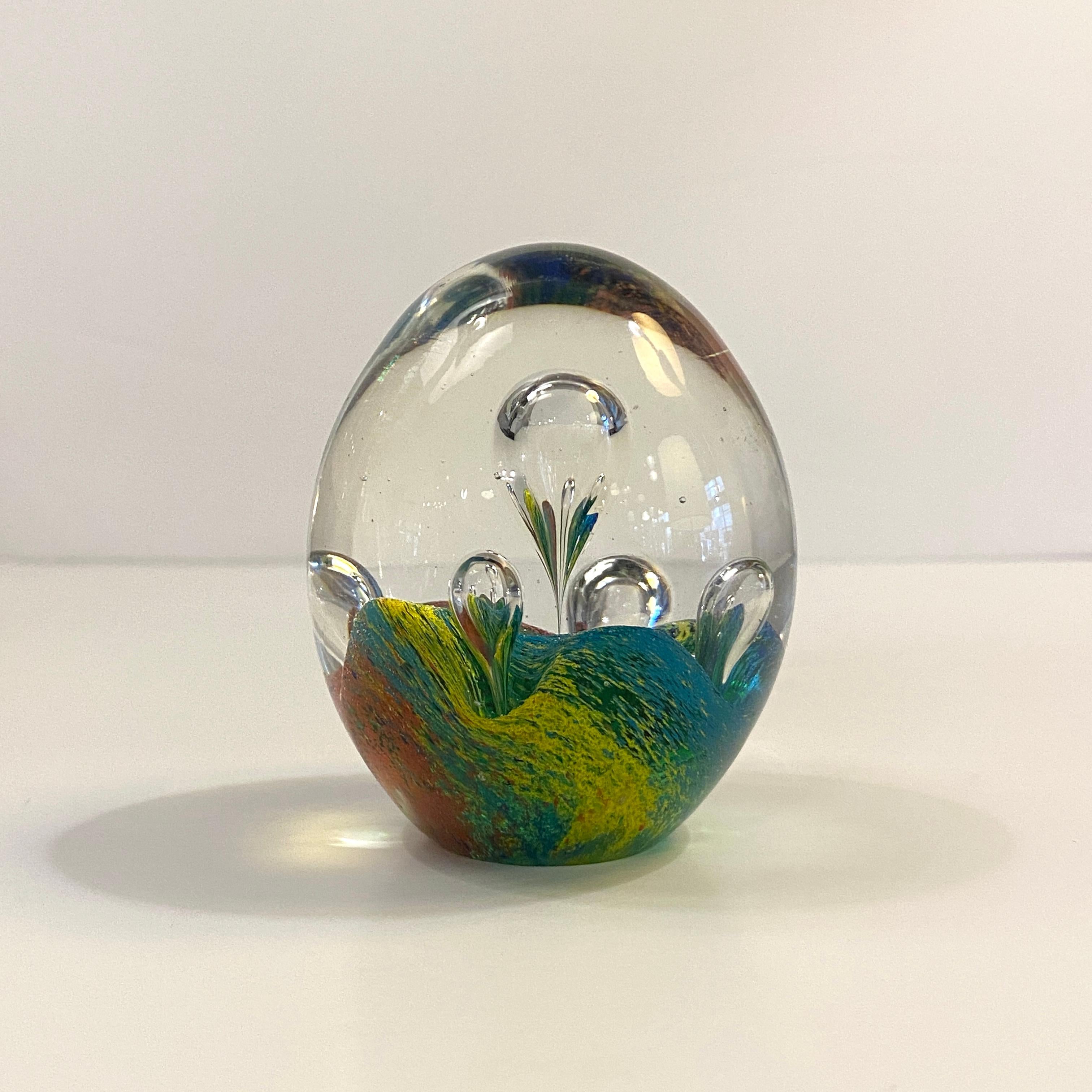 Oval shaped, artisan-made, hand-blown, Italian Murano art glass paperweight features a bed of colorful teal, blue, yellow, and red with clear bubbles rising resembling hot air balloons. It's a wonderful decorative object or desk paperweight.