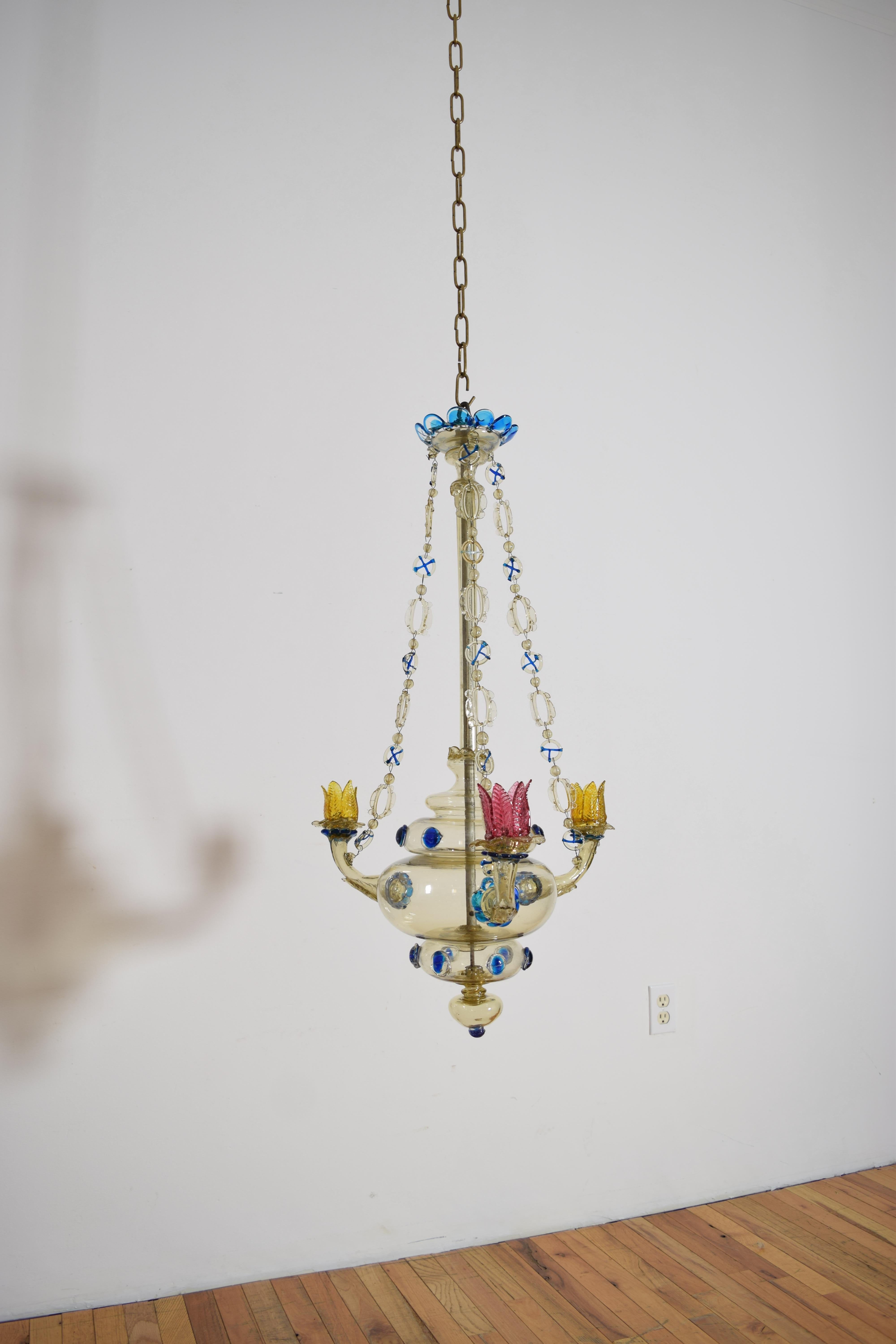 un fino y raro ejemplo de soplado de cristal de Murano, el accesorio tiene un estandarte central debajo de un dosel que emite tres cadenas de cristal que se conectan a brazos fundidos a  el cuerpo consta de cinco secciones, la mayoría con detalles