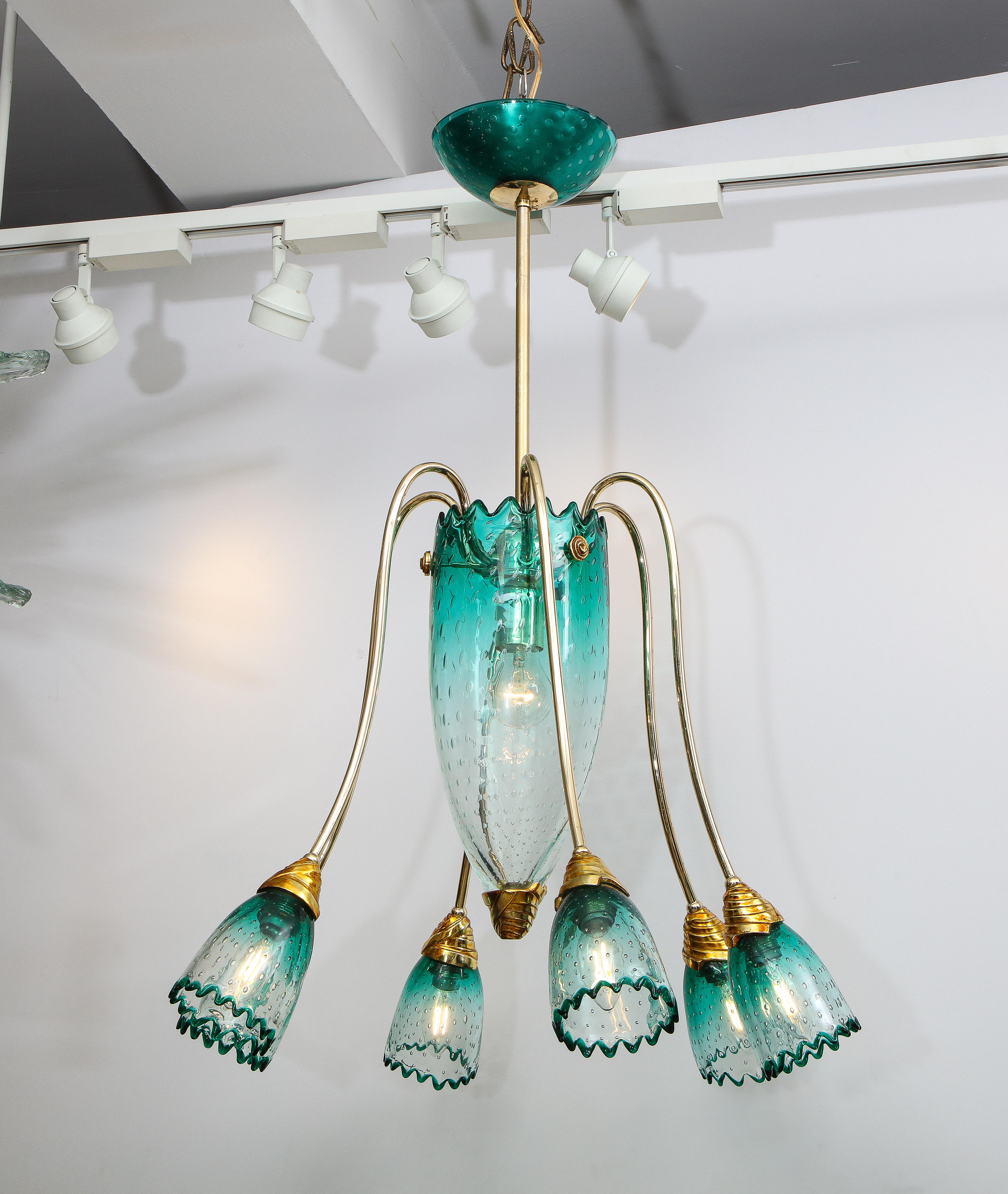 An elegant Italian Murano glass chandelier attributed to Seguso with controlled bubbles in teal blue which fades to clear, with a central upright elongated conical body with six curvilinear brass arms ending in bell shaped shades, all the edges