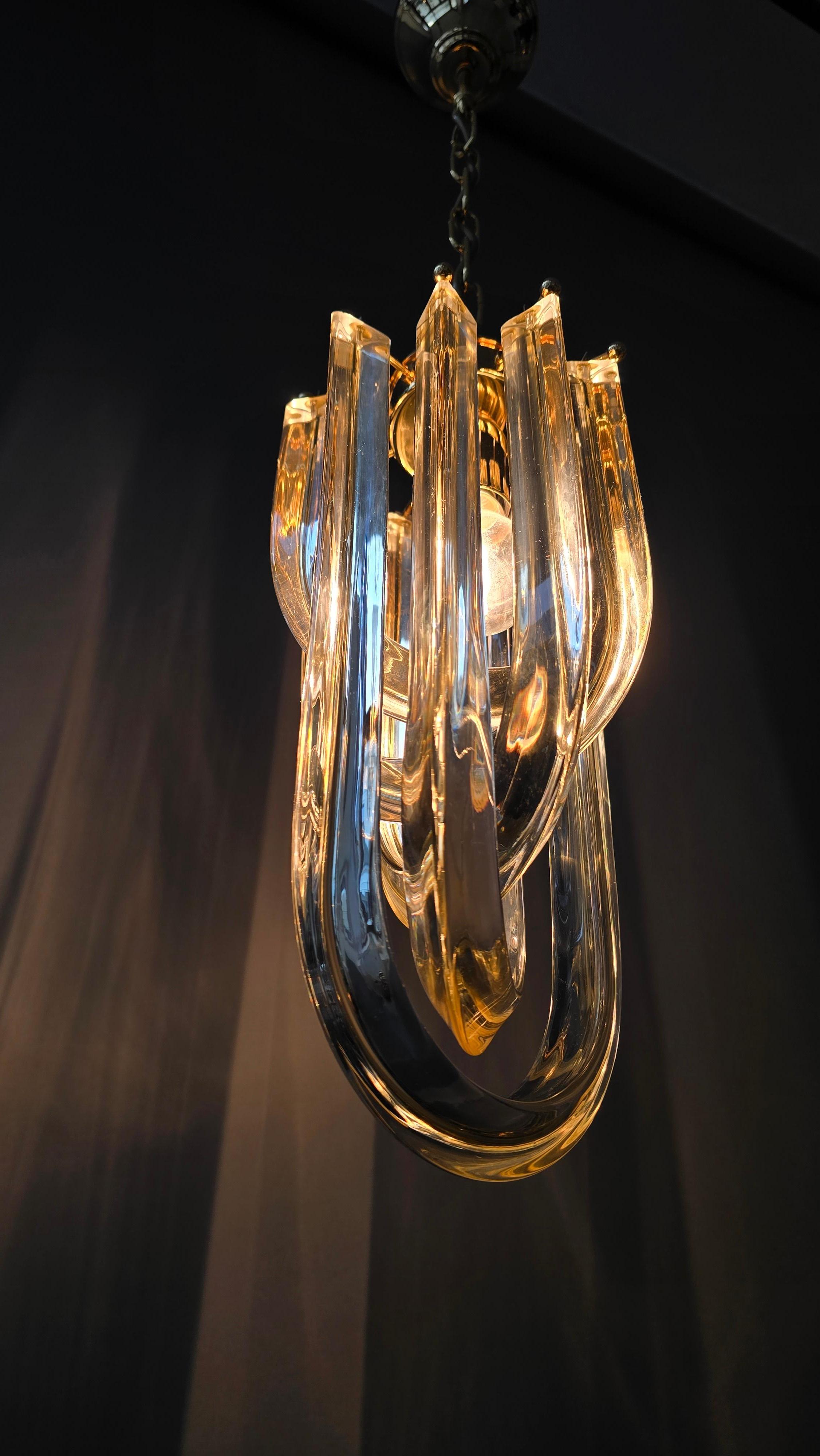 Pendente italiano di Murano degli anni '70 in stile Venini, realizzato con spessi elementi in cristallo a forma di U e una montatura in oro lucido. Luce calda e chiara e artigianato raffinato. 

Elegante pendente di Murano degli anni '70 costruito