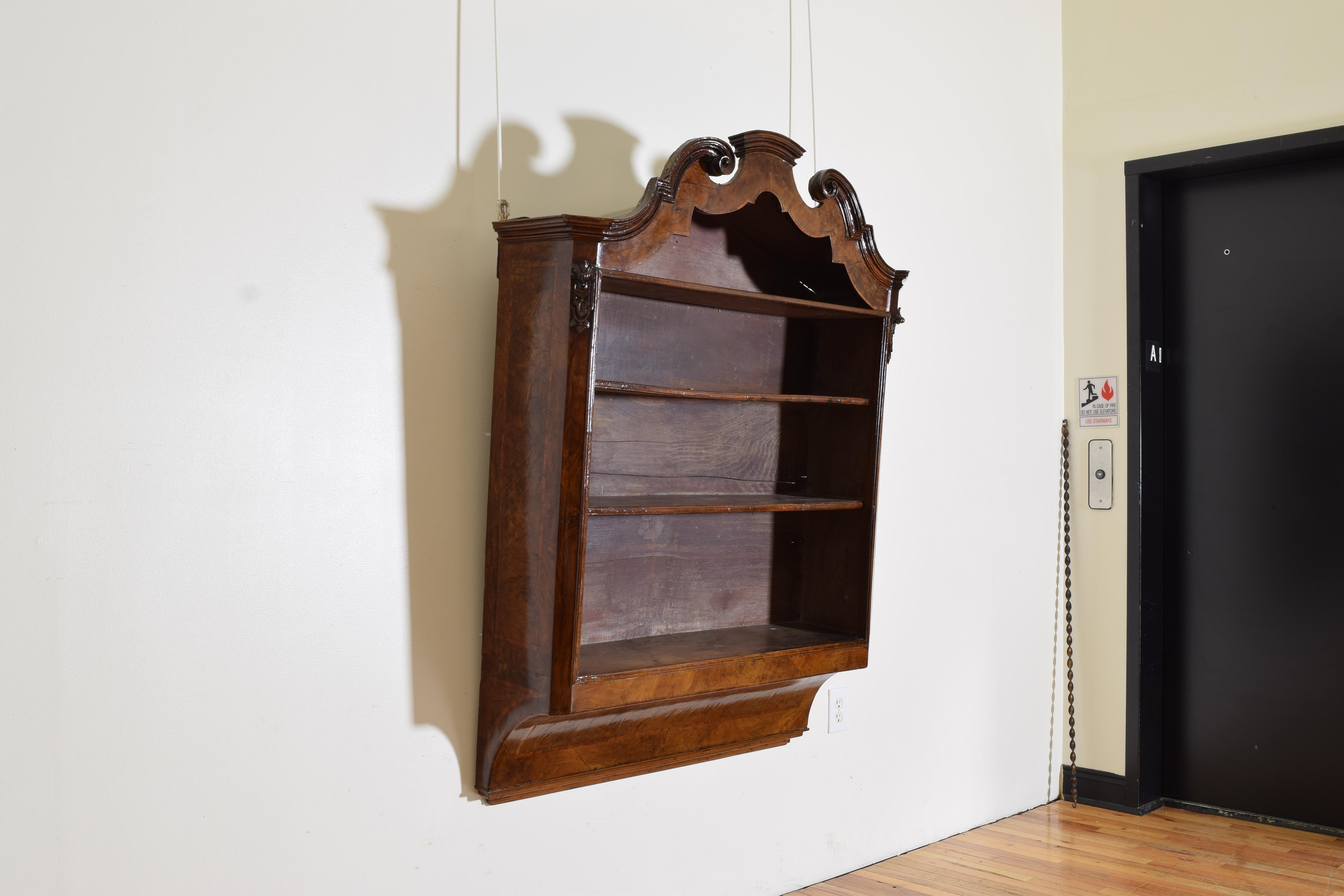 Having a shaped and carved pediment in the early Georgian style this Italian hanging wall shelf has four levels with beautifully figured walnut veneers, the bottom is curved inward and ends in stepped moldings