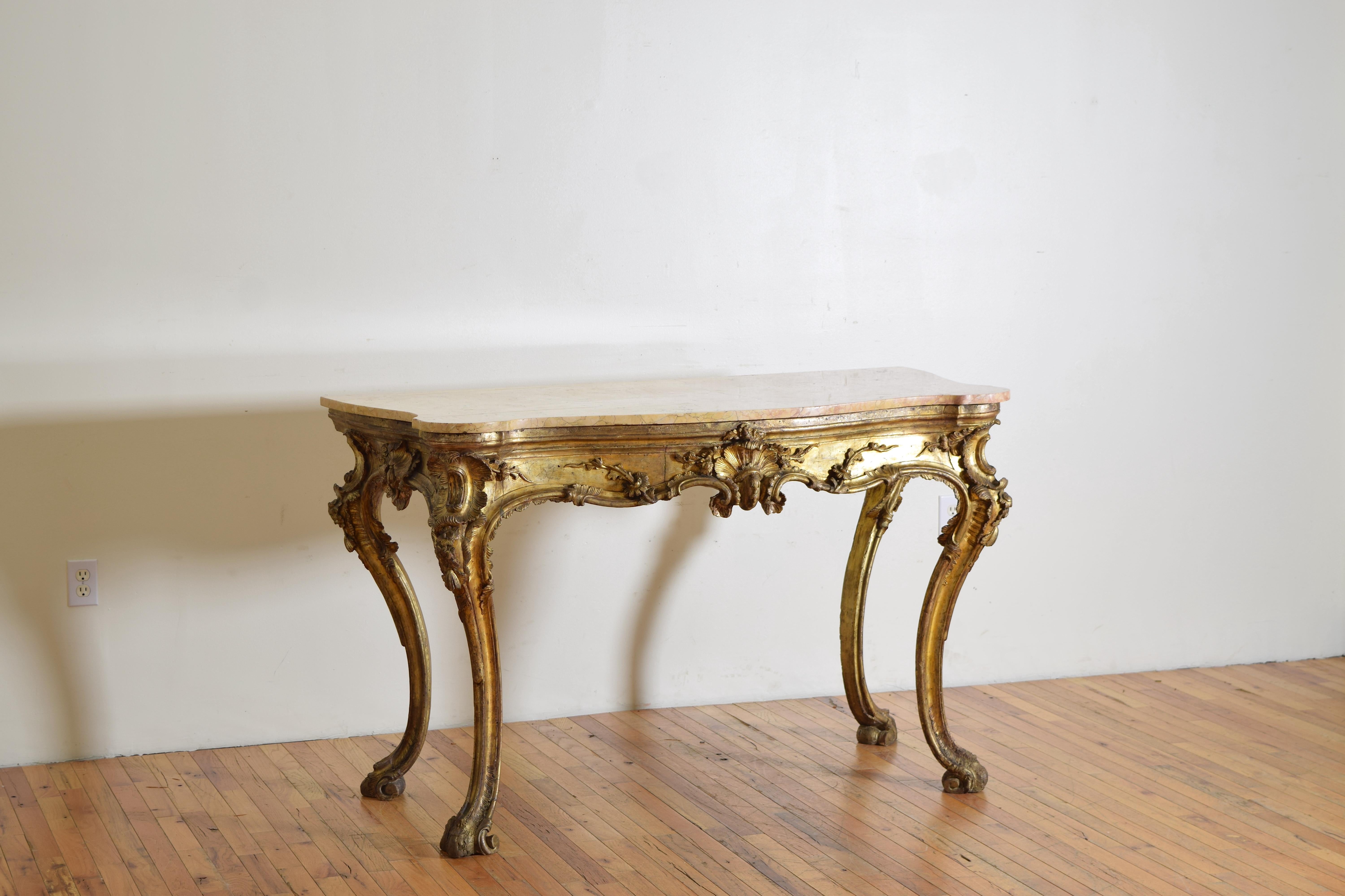 The Verona Antica serpentine shaped marble top resting atop a conforming frame of carved wood and covered in Mecca (silver gilt) with a time acquired gilt patina, the carvings of shells, vines, scrolls, and flowers, raised on dramatic cabriole legs