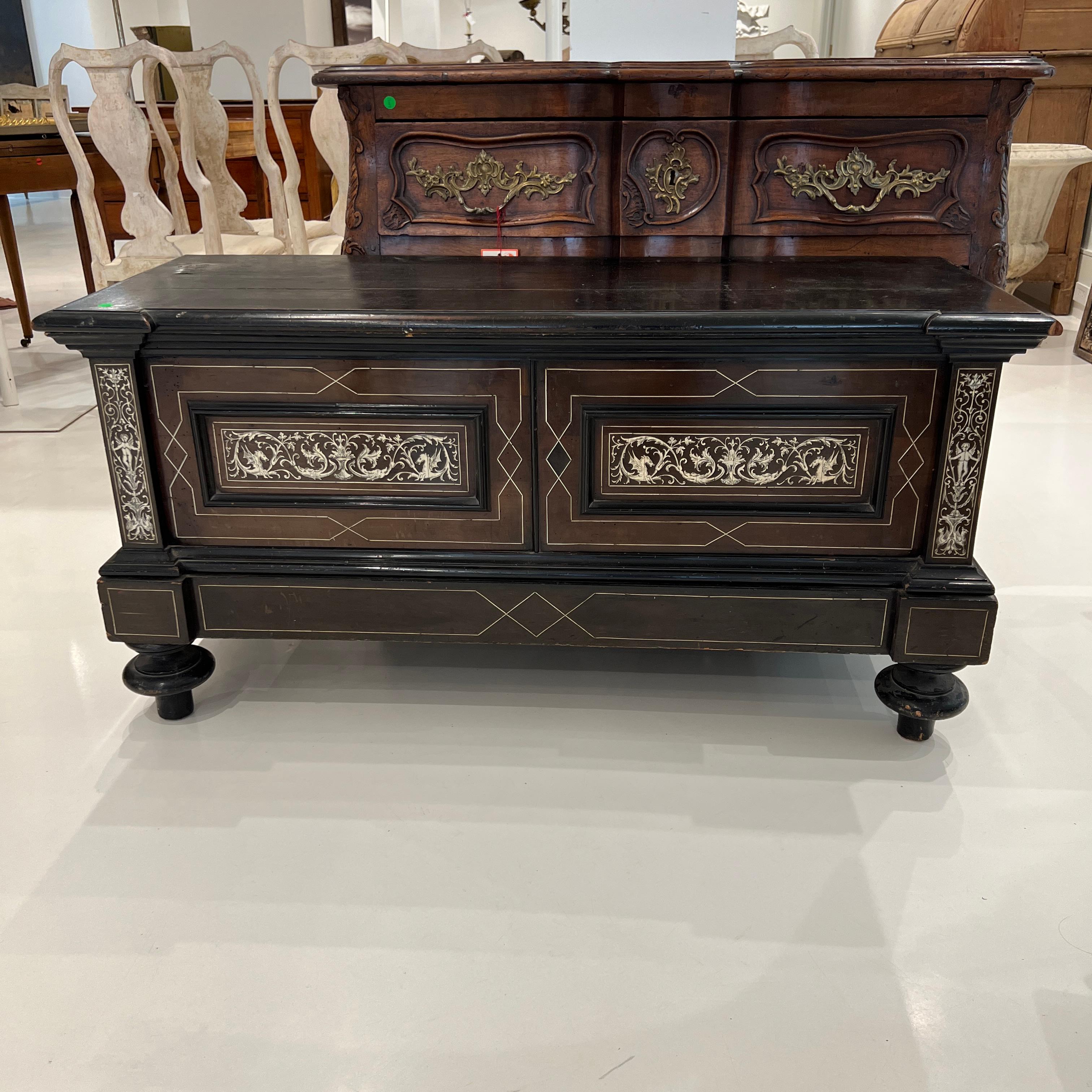 Black trunk with copious detailing and ornamentation in inlay bone.  Graceful turned feet at the front.  Fits perfectly at the foot of a bed.