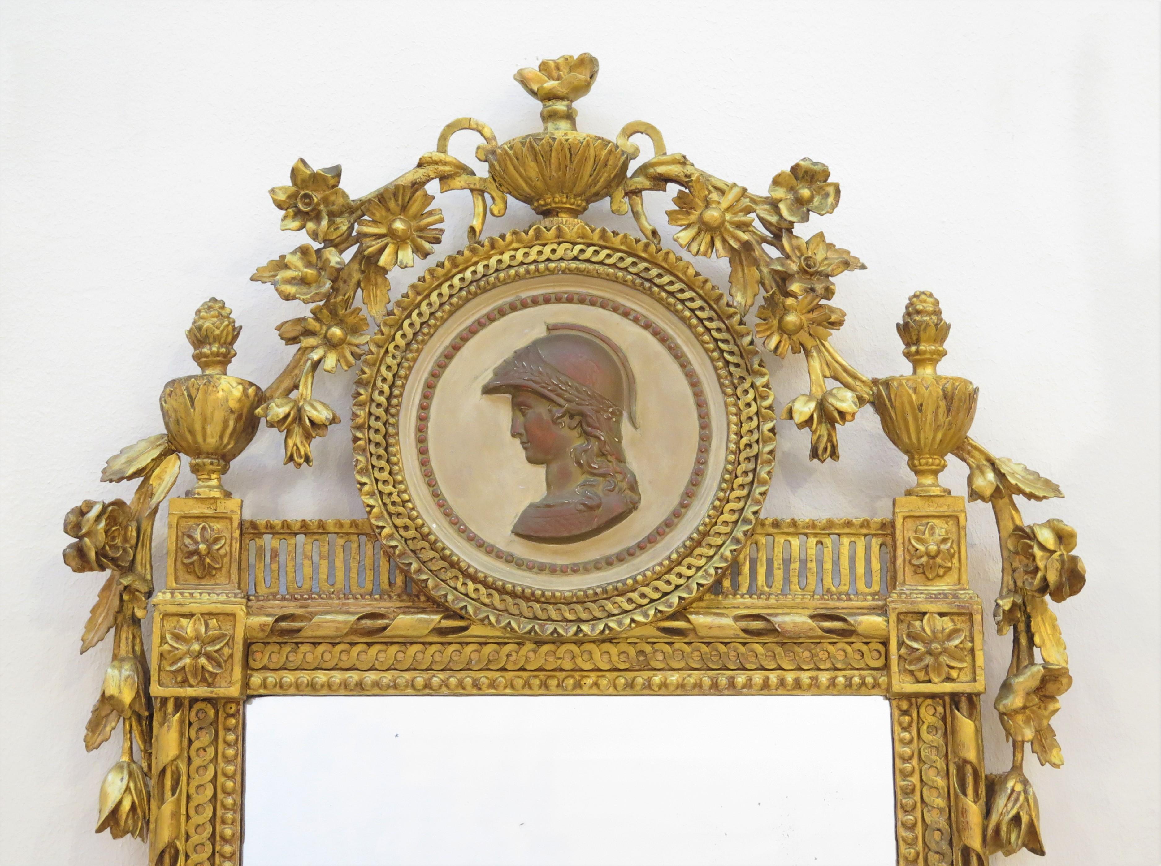 a Neoclassical giltwood pier glass / pier mirror adorned with a round bas-relief portrait medallion (terra cotta in color) of a Roman soldier at its crest, topped and flanked by leafy urns and having flowering vines (with leaves) throughout its very