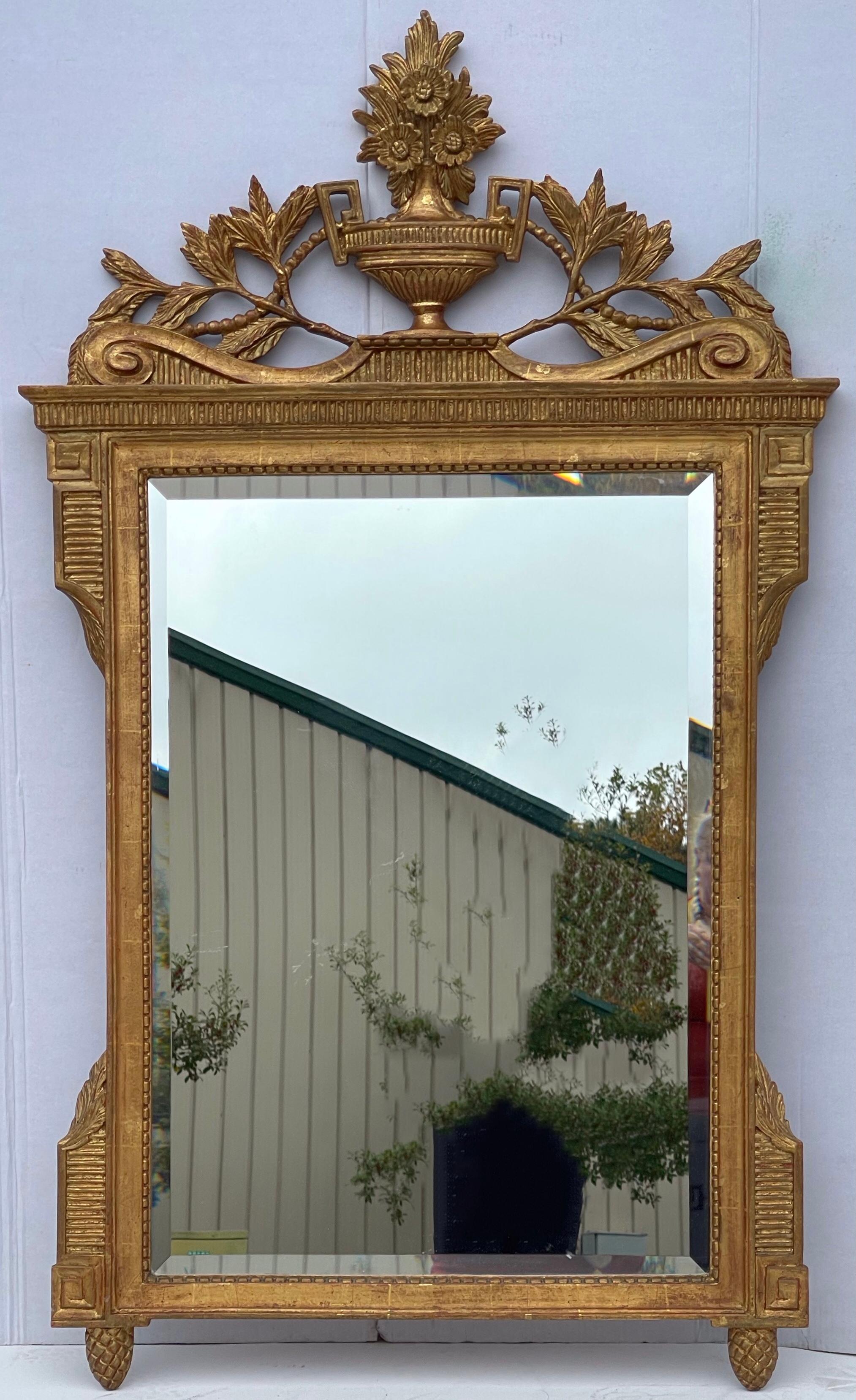 These are beautiful! This is a pair of Italian neo-classical style carved giltwood mirrors. They were crafted for Mirror Fair and distributed out of New York. The pediment is gorgeous with an urn that has a floral spray and Greek key form handles.