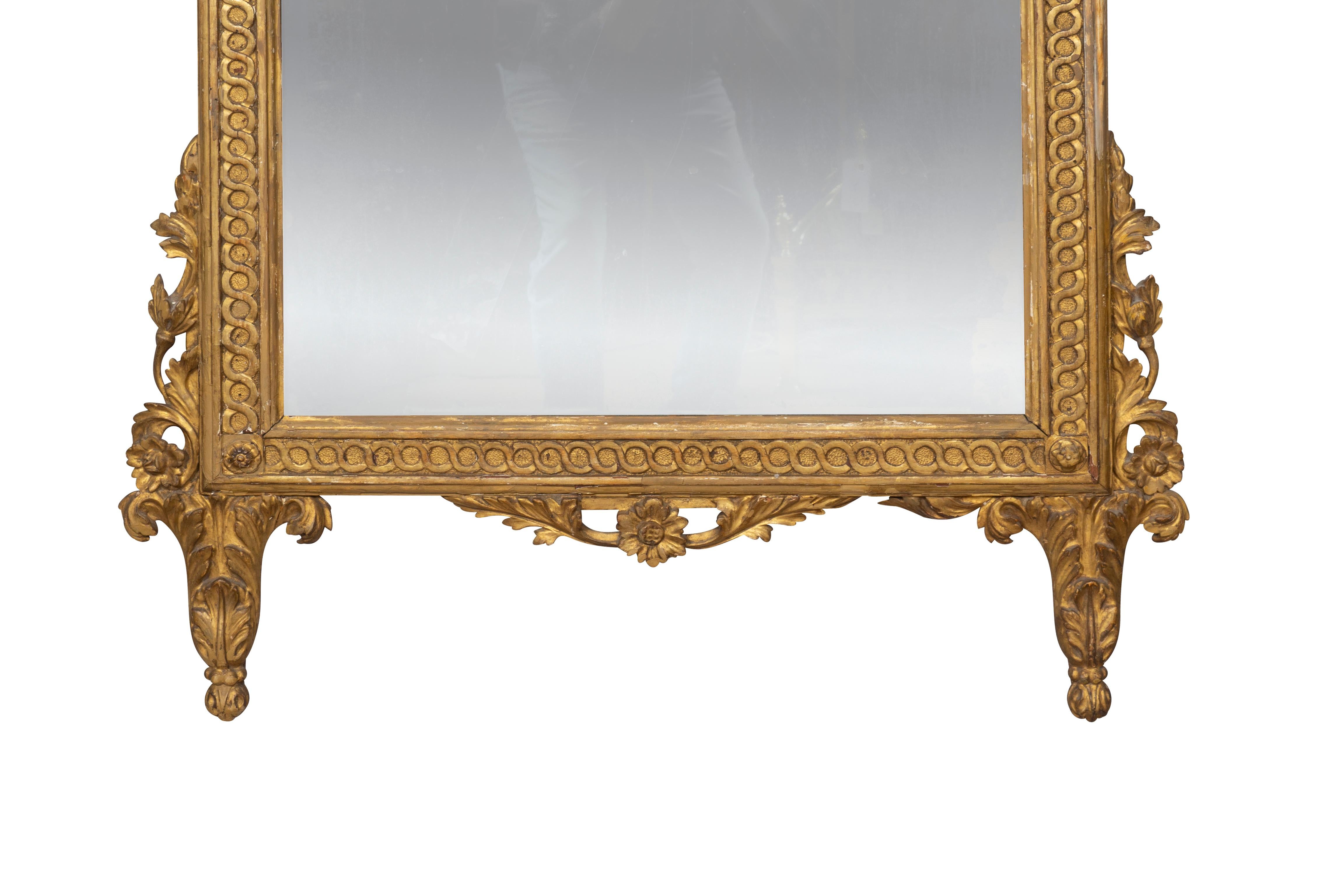 With original wonderful surface gilding. The crest with urn of flowers and trailing arabesques over an original distressed mirror plate that we will replace if requested. The frame with guilloche border. The bottom of the mirror with leaf form feet.