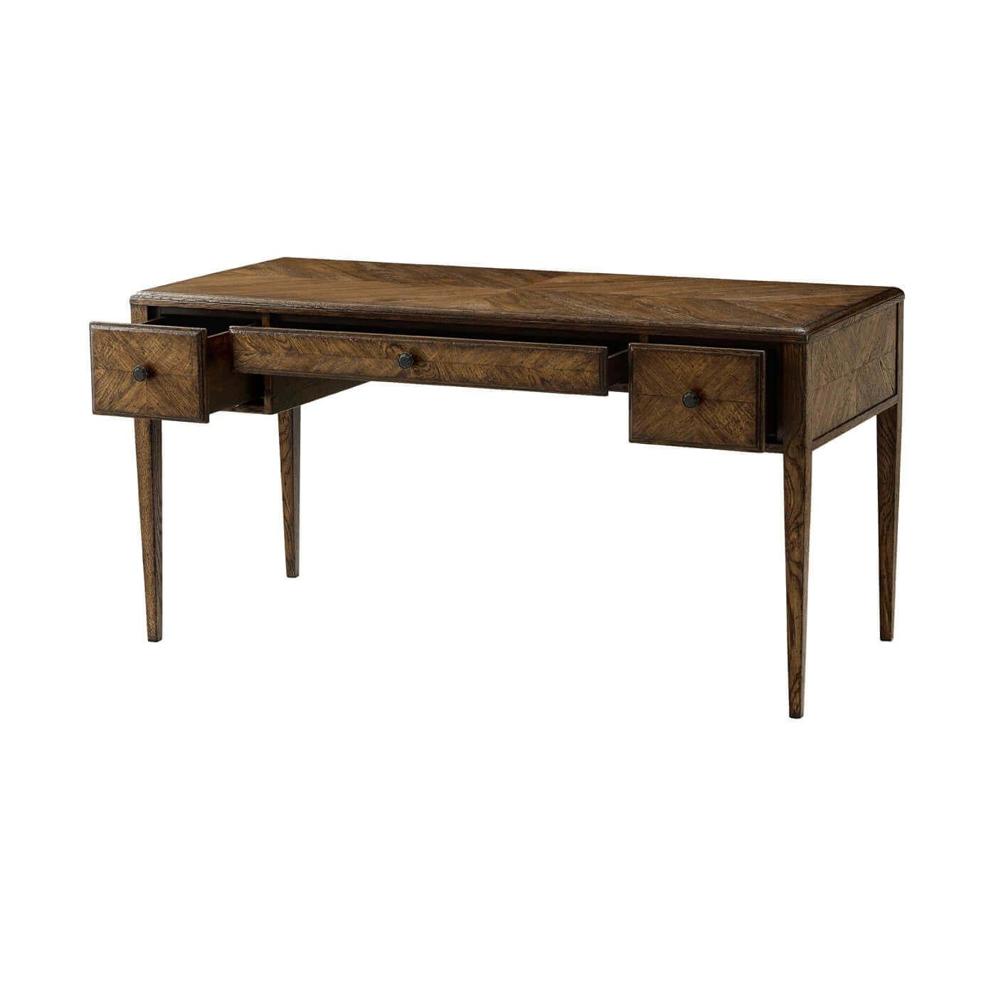 An Italian Neo-Classic style oak parquetry desk with a starburst patterned oak parquetry top to bottom. It has a central drawer flanked by two further additions. It rests on tapered legs. It has an oak finish complimented with Verde Bronze finished