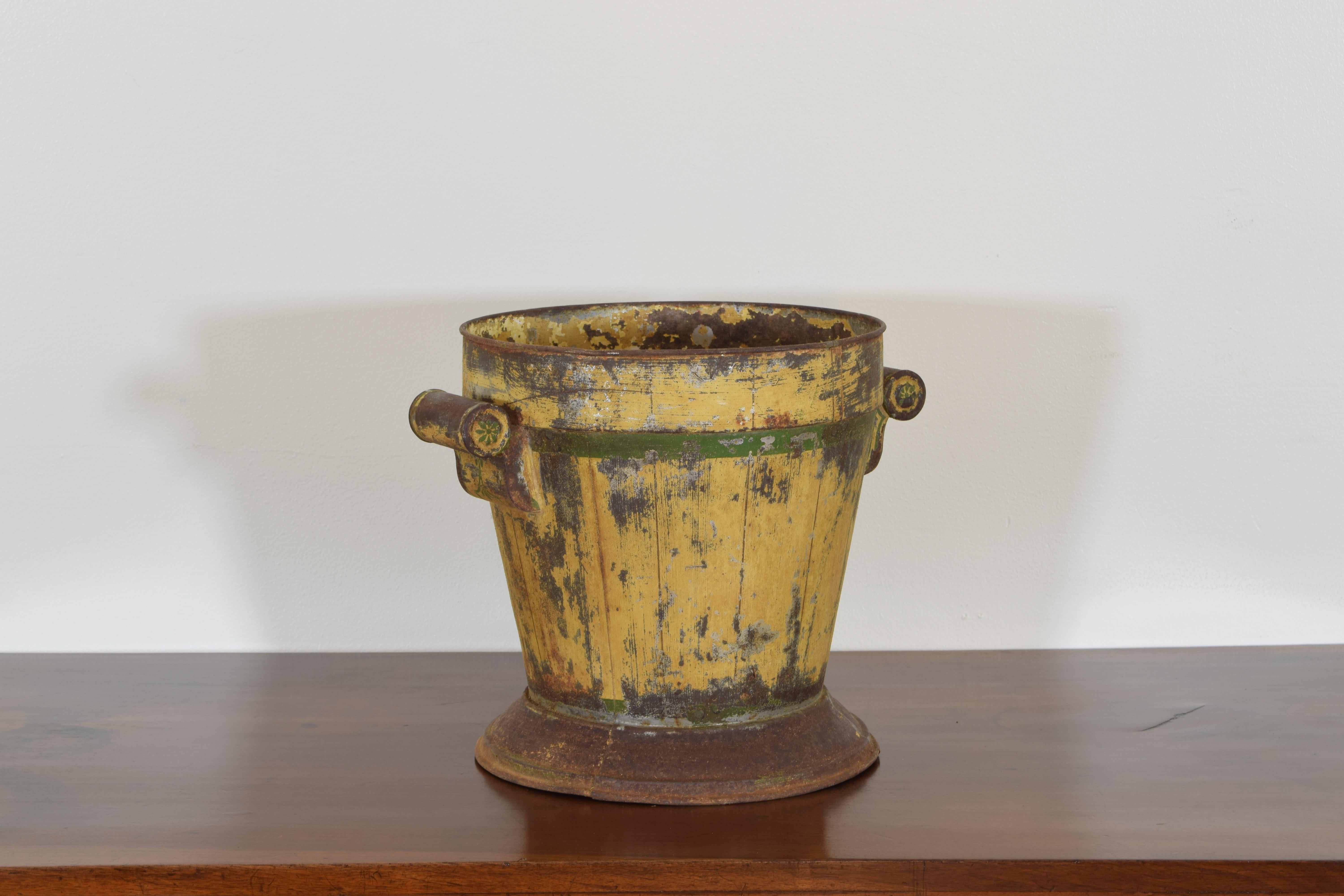 In the neoclassical taste with yellow and green painted tole surfaces, the tapering body surmounted atop a plinth base and having rounded handles, the interior with the original pierced liner, the bottom rusted open in areas.