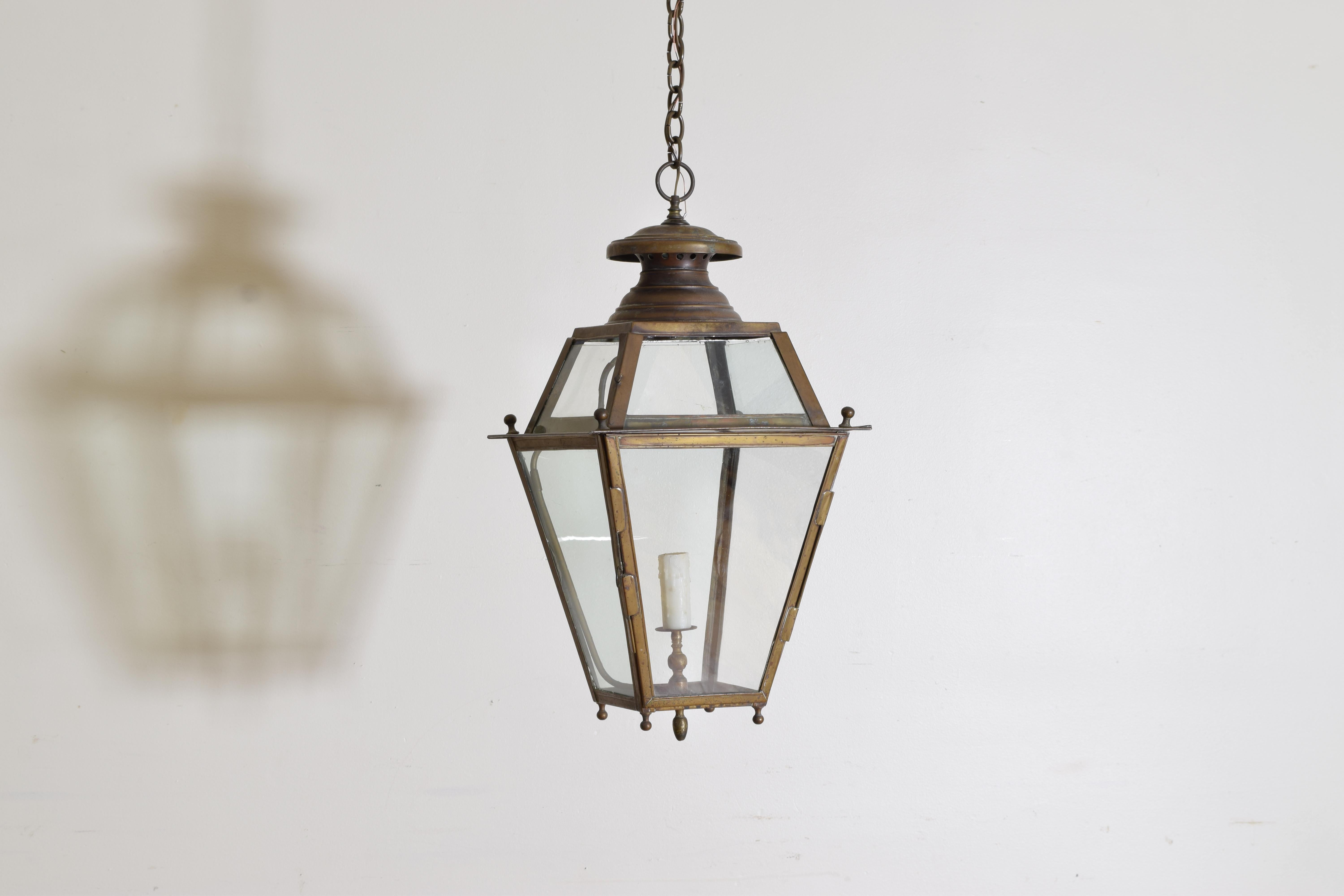 This four sided tapering brass lantern has 8 glass inserts and a shaped top with large finial, retaining its original gas line and spigot but now electrified, the bottom with small brass feet and a central terminal.